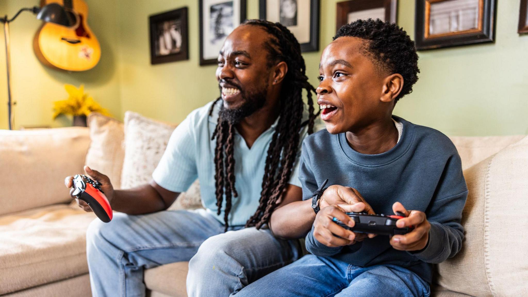 a father and son smiling and playing video games together on the sofa
