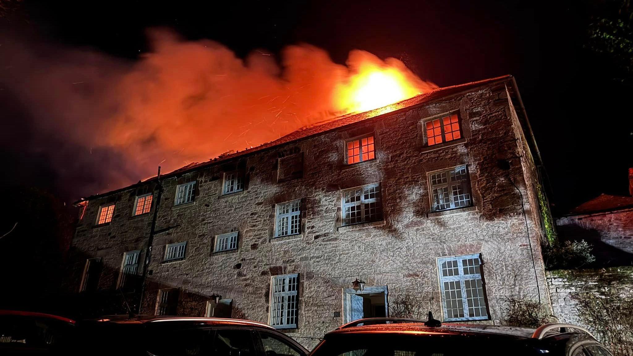 A three-storey stone-brick building is on fire at night with the majority of the flames on the third floor.