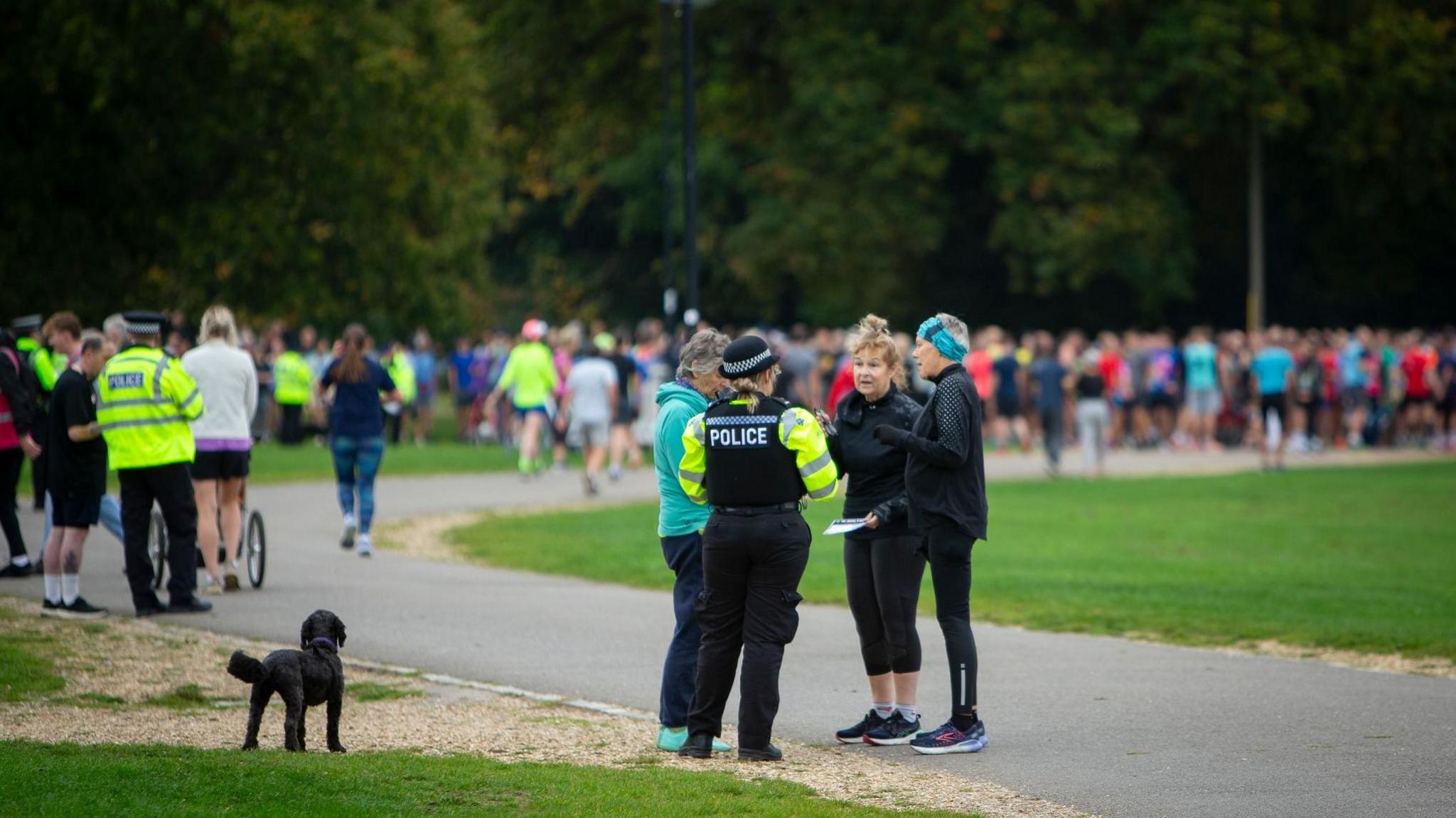 A large gathering of runners on Southampton Common. In the foreground are two police officers in hi-viz jackets talking to two separate groups of runners.