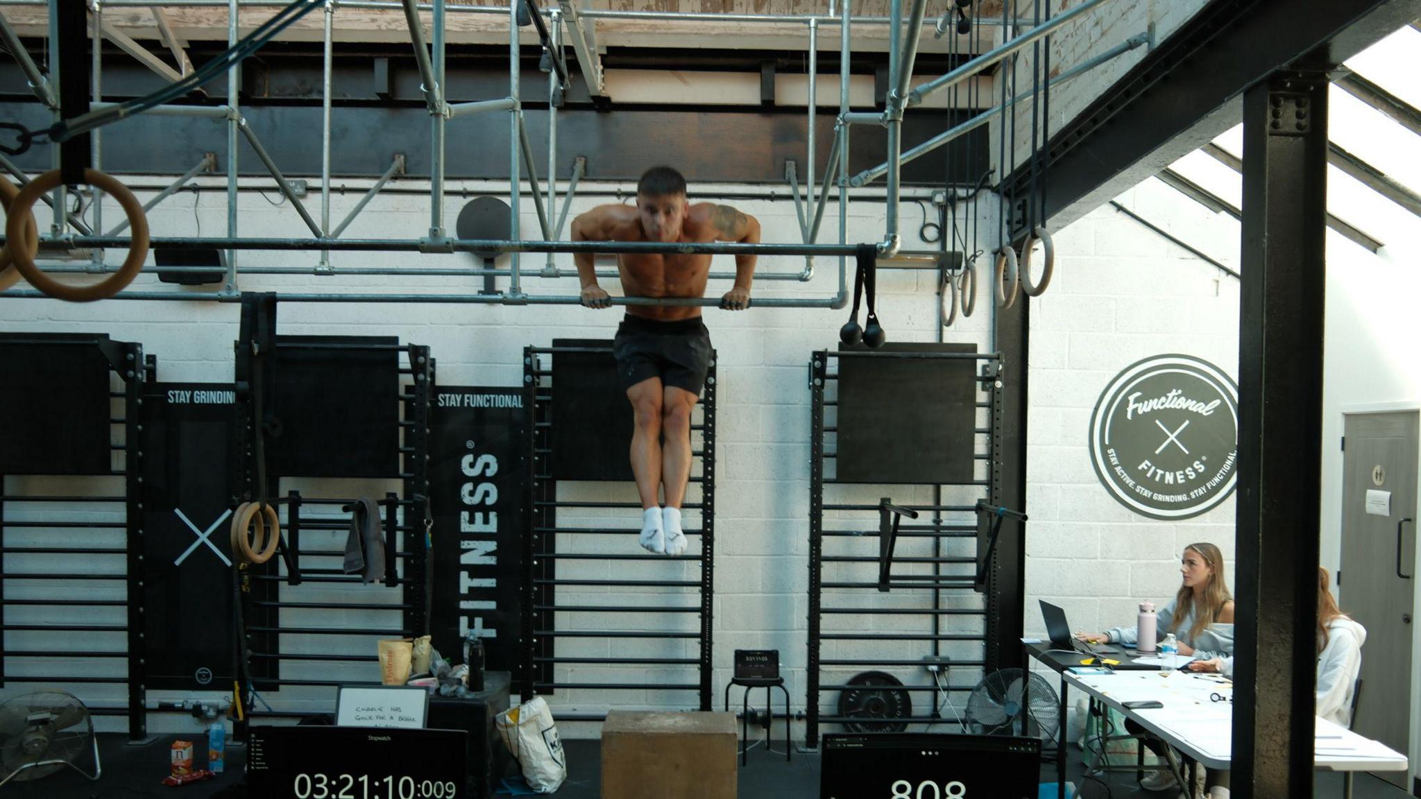 Man on a bar in the air in a gym topless doing muscle-ups 