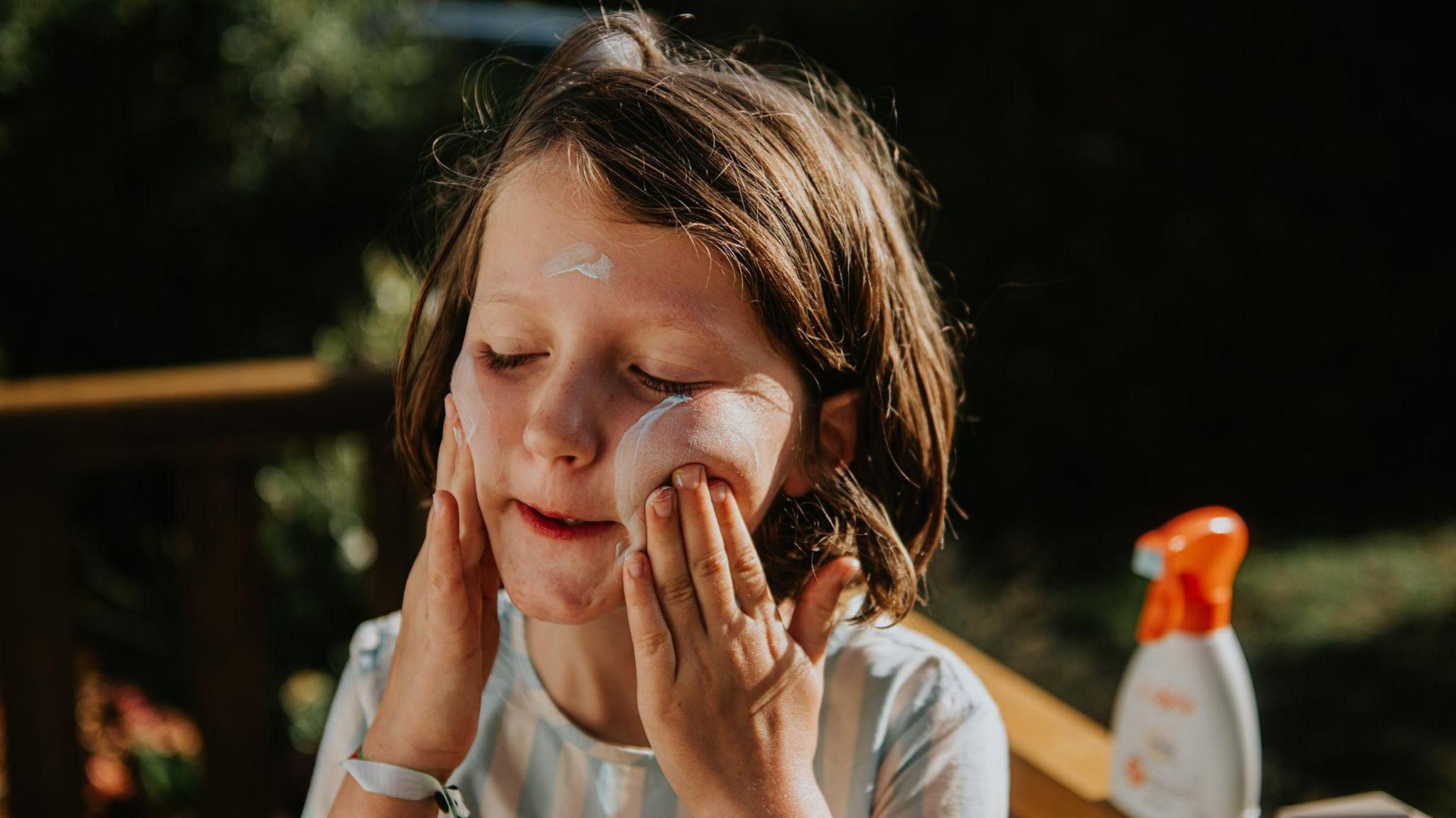 A child is carefully applying sunscreen on her cheeks