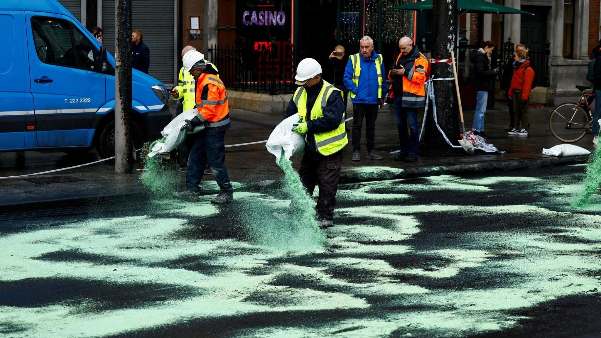 Workers spread green dust on a road to soak up oil