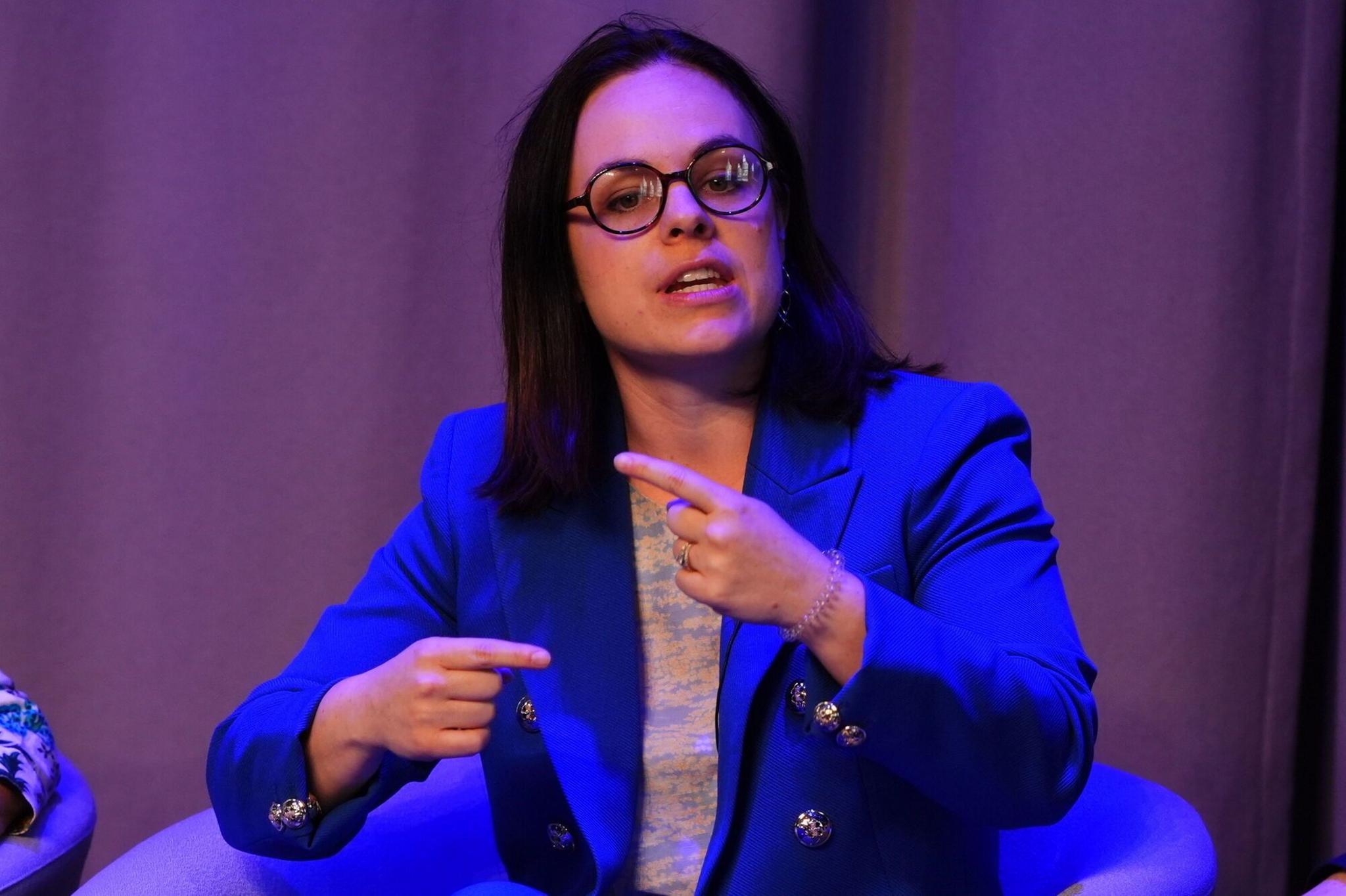 Kate Forbes speaks on stage. She sits in an armchair and wears a blue blazer, black glasses and gestures with her hands.