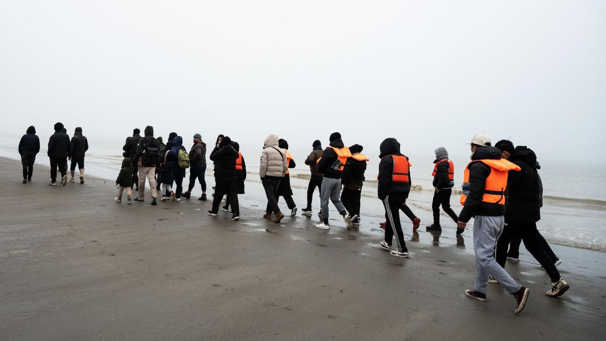 A group of migrants, some wearing lifejackets walk along a beach in France before taking a boat to the UK.