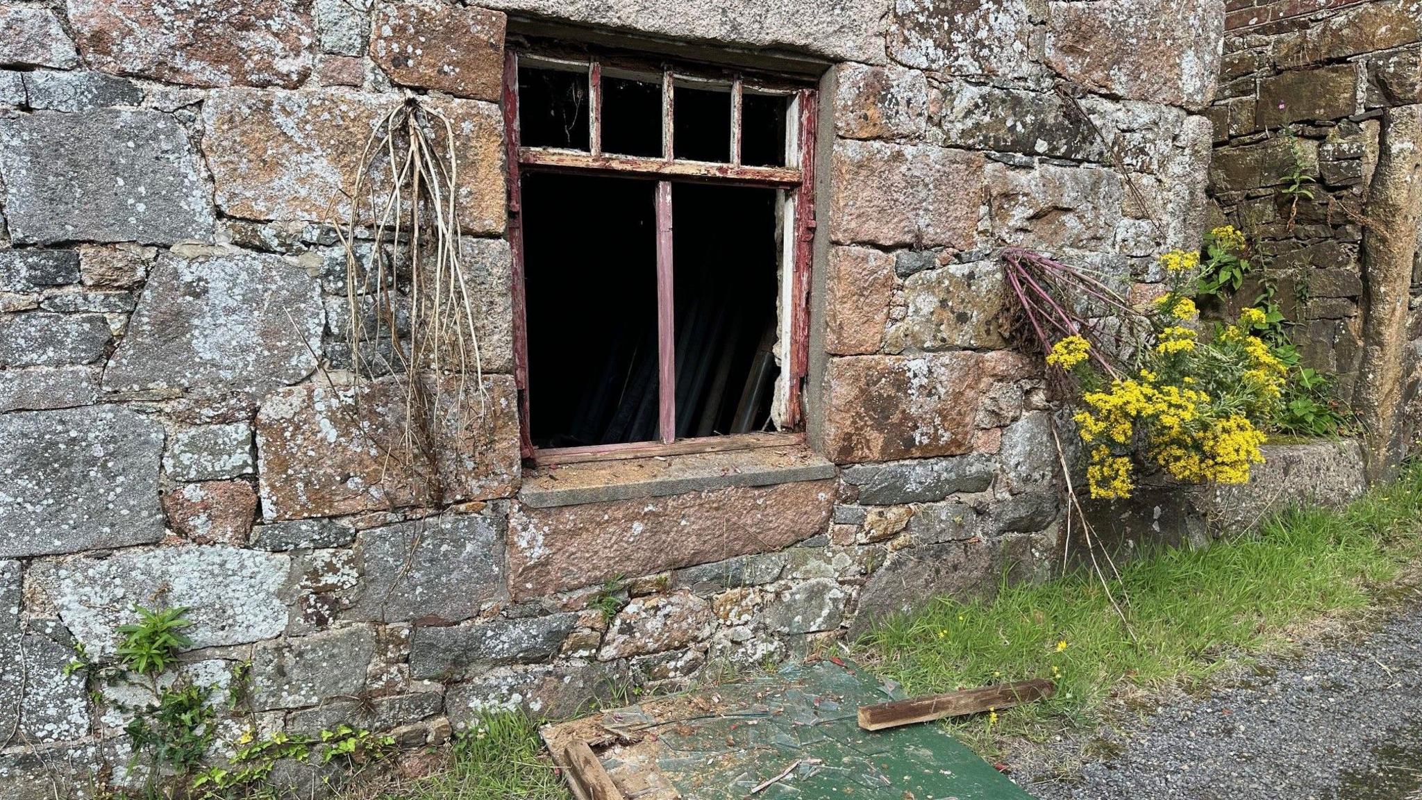 A large ground floor window with its glass smashed and lying on the ground under it