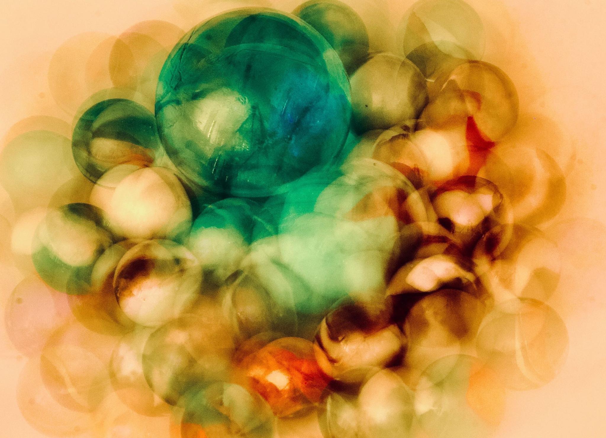 A blurred photograph of marbles. The main colours are green and gold with a hint of brown and orange.