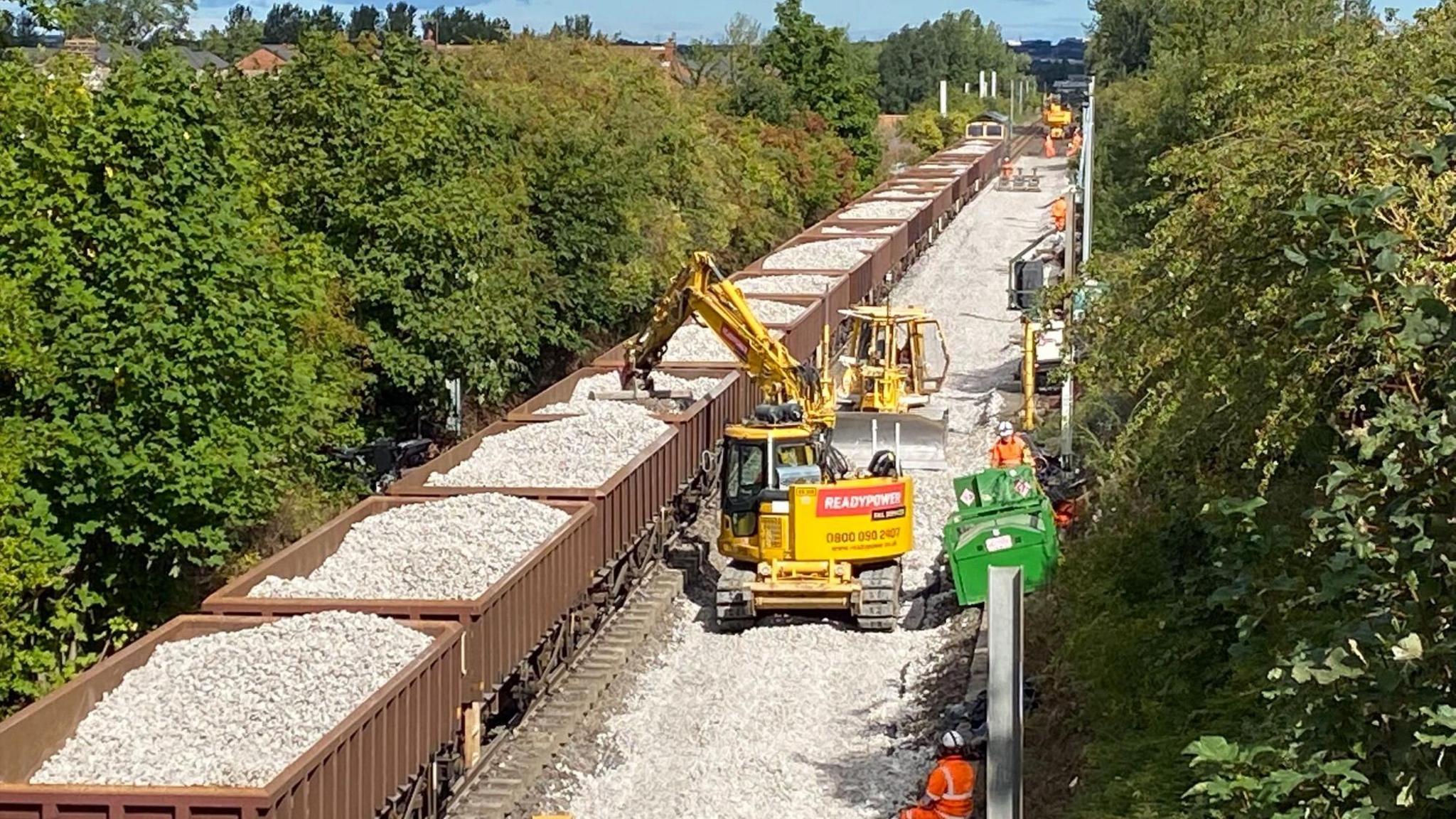 Diggers removing gravel and stones from the back of a train. 