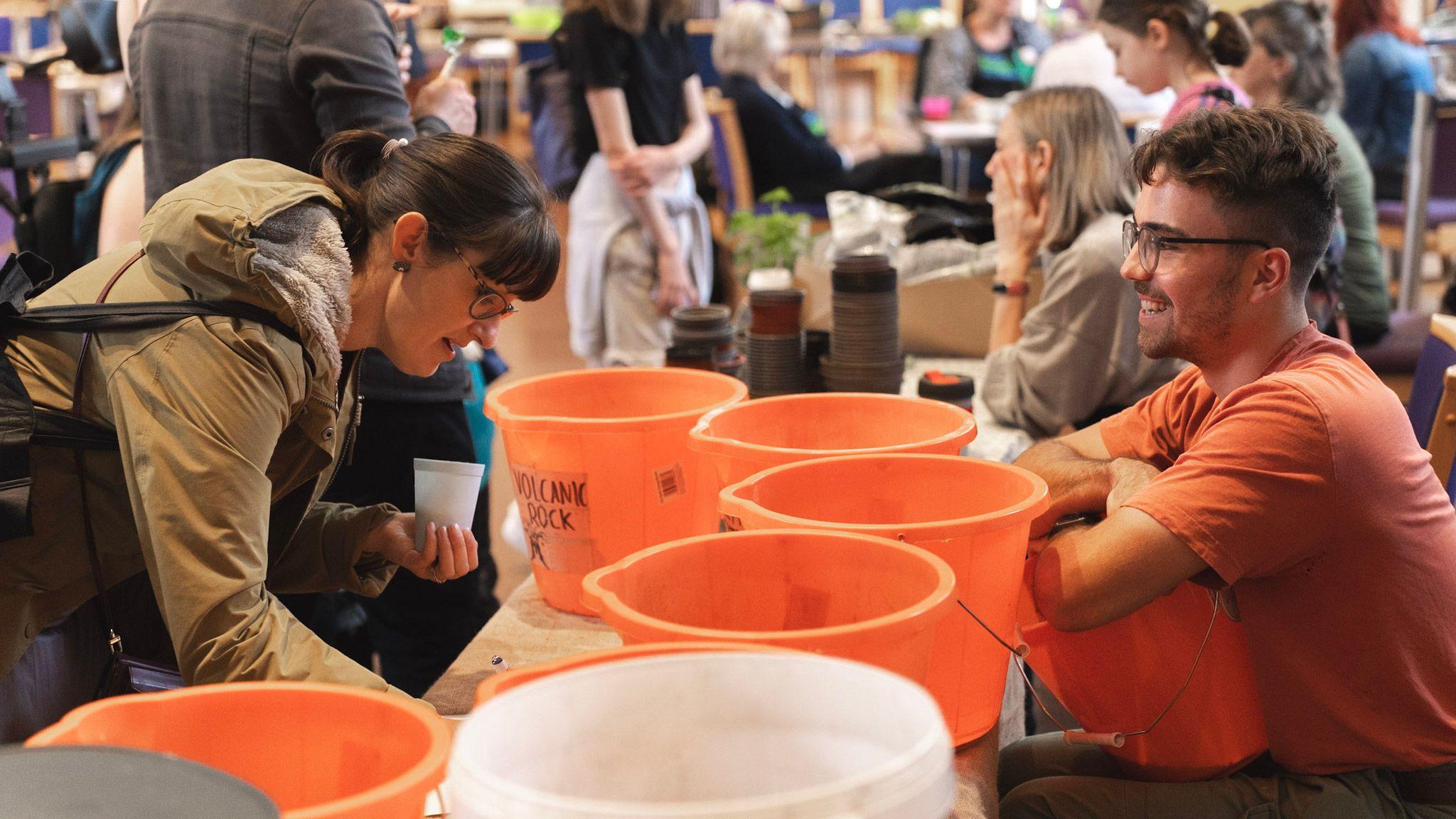 Two people smile at each other over the top of a line of orange buckets at the BS3 Jammin event at St Paul's Church in Southville