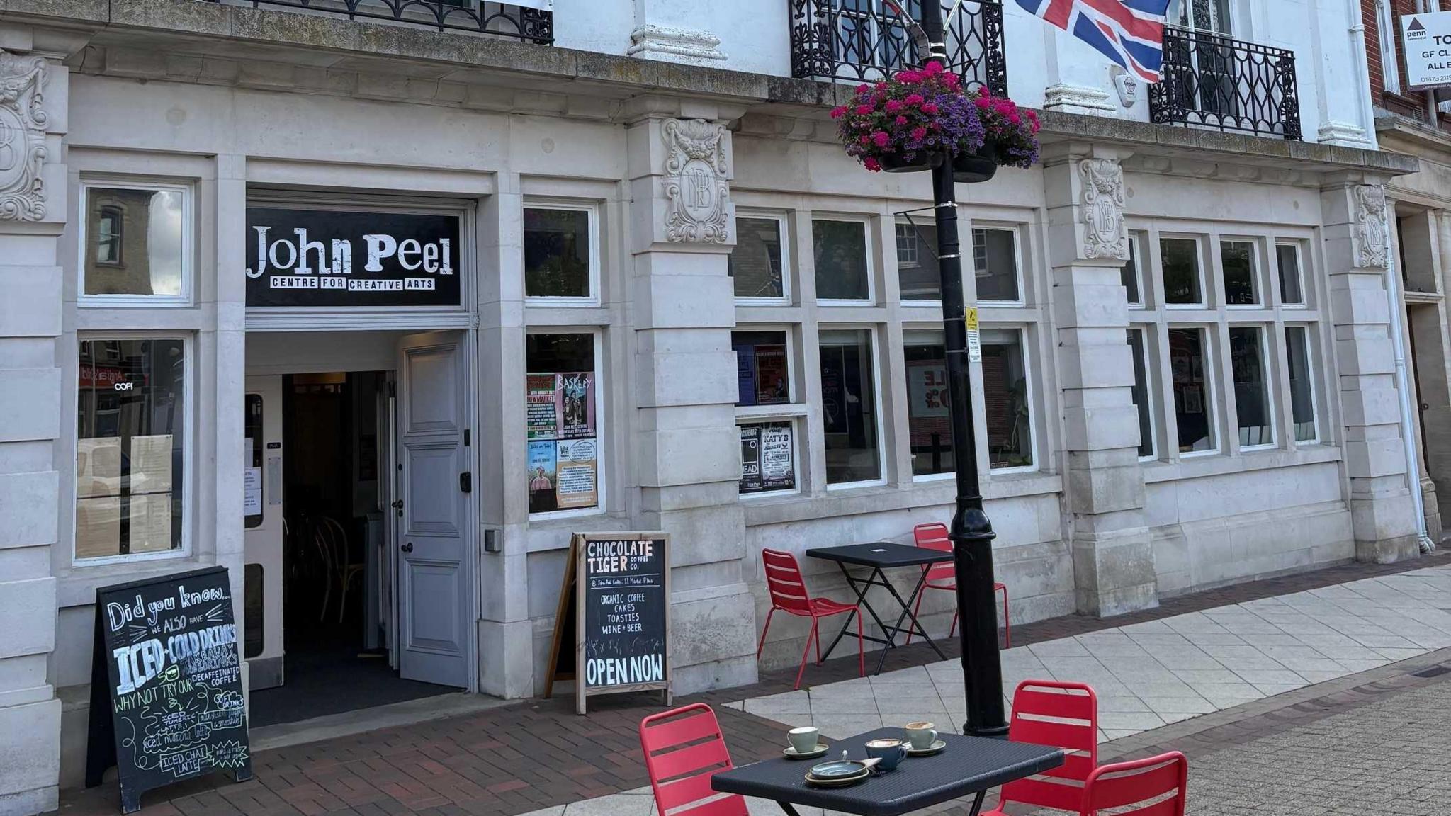 A view of the exterior of the John Peel Centre in Stowmarket. Chairs and tables rest outside.