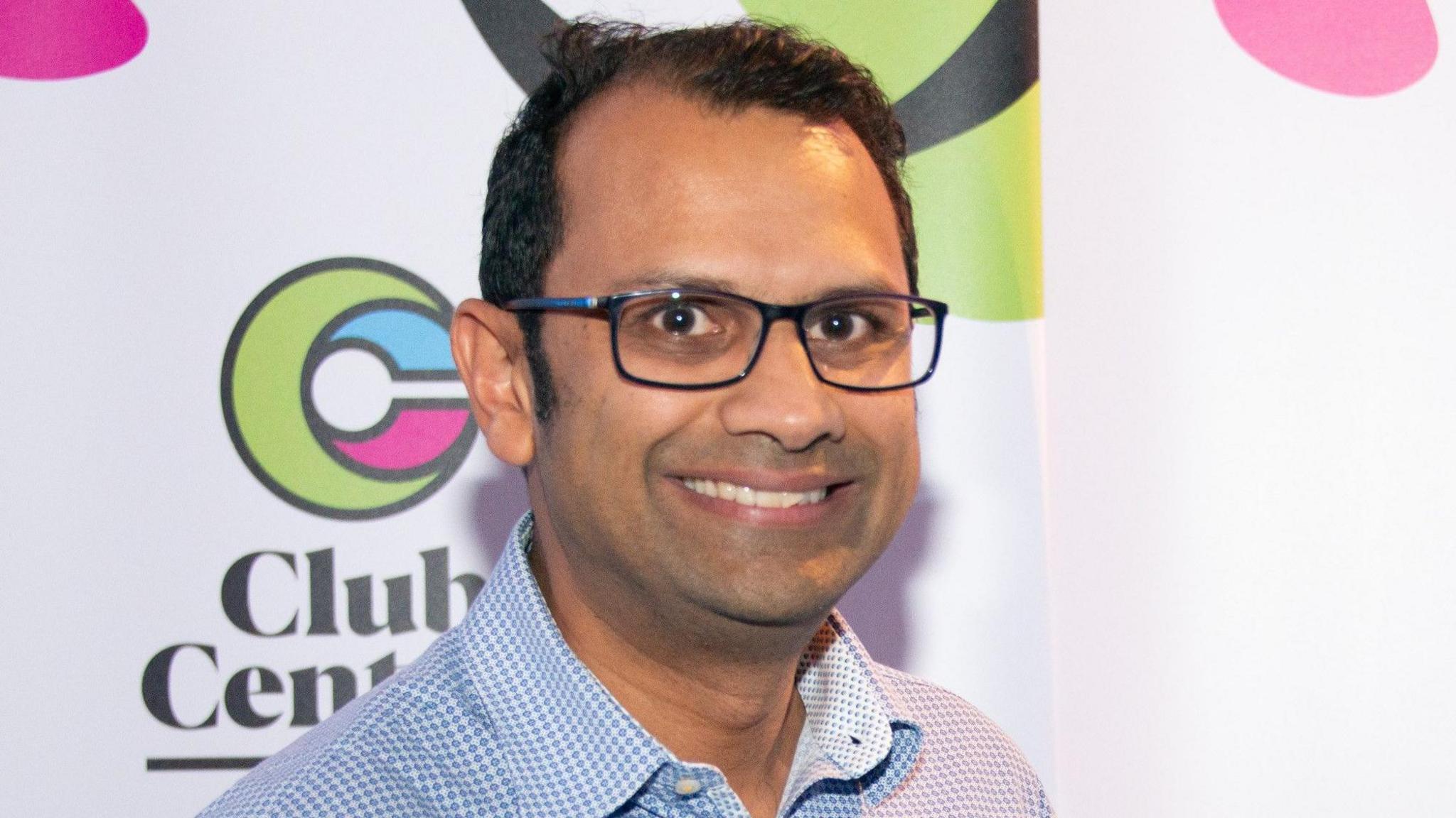 Head and shoulders shot of Panash Shah smiling, wearing a blue and white checked shirt.