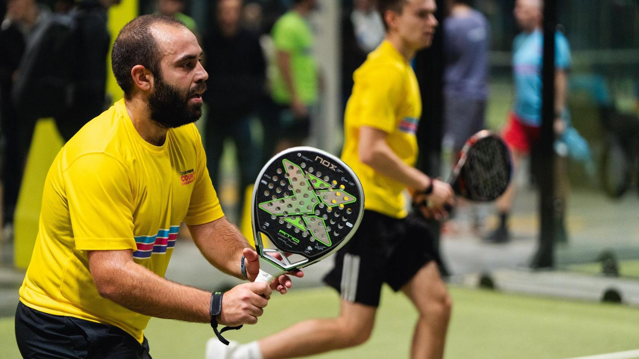 Two men wearing yellow t-shirts holding sports rackets