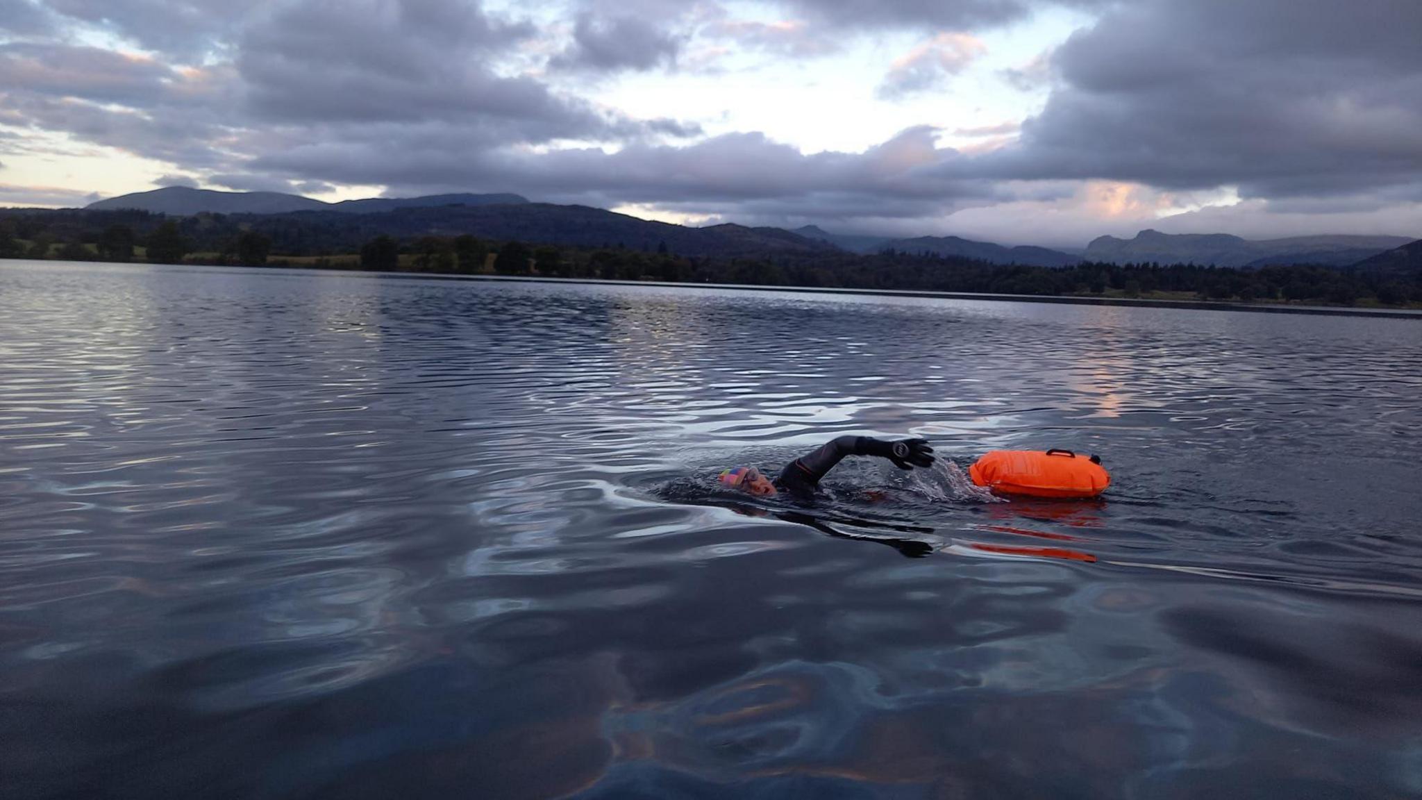 A woman swimming in a vast lake followed by her orange safety float