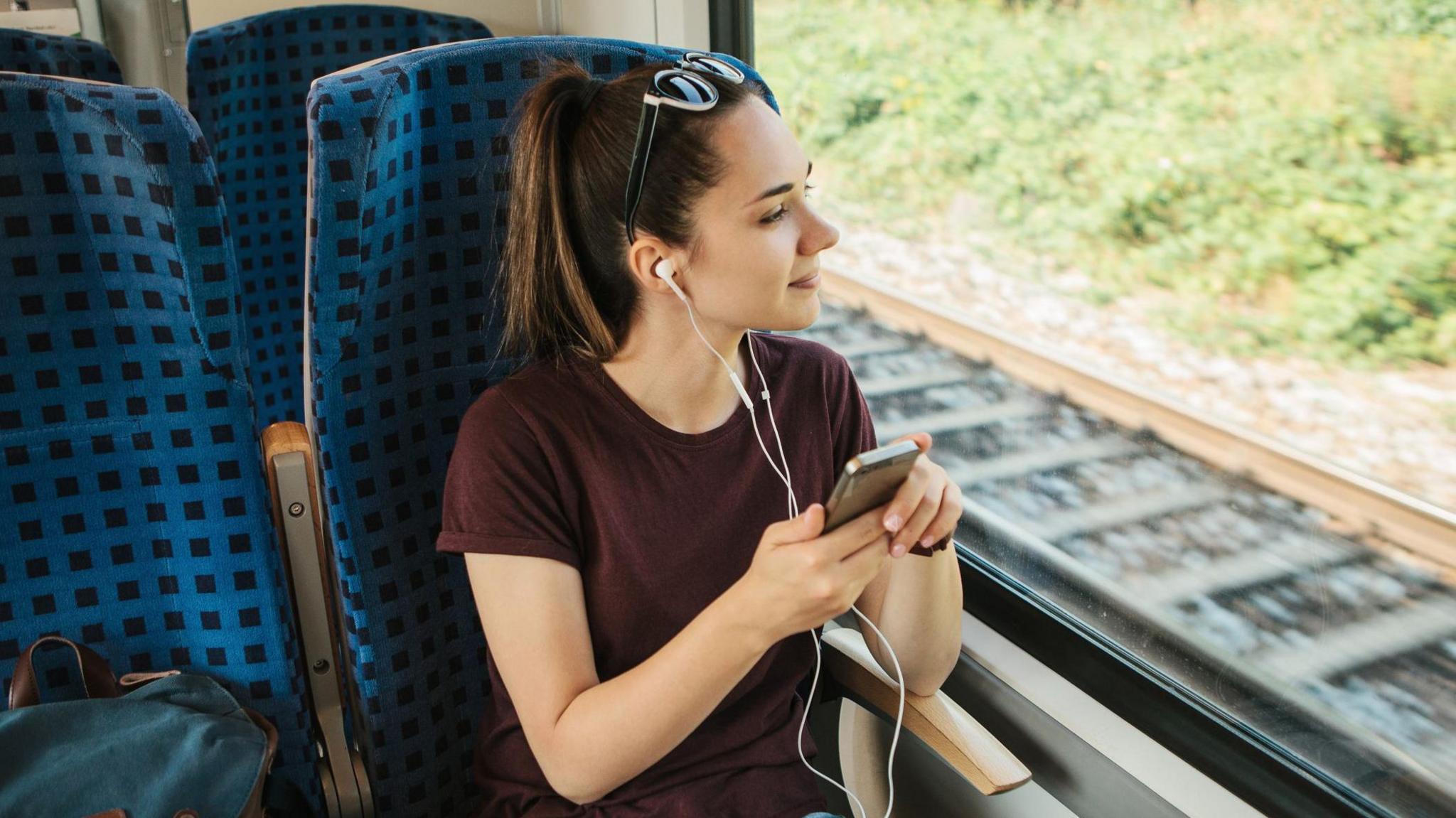 A teenage girl sitting on a train listening to headphones 