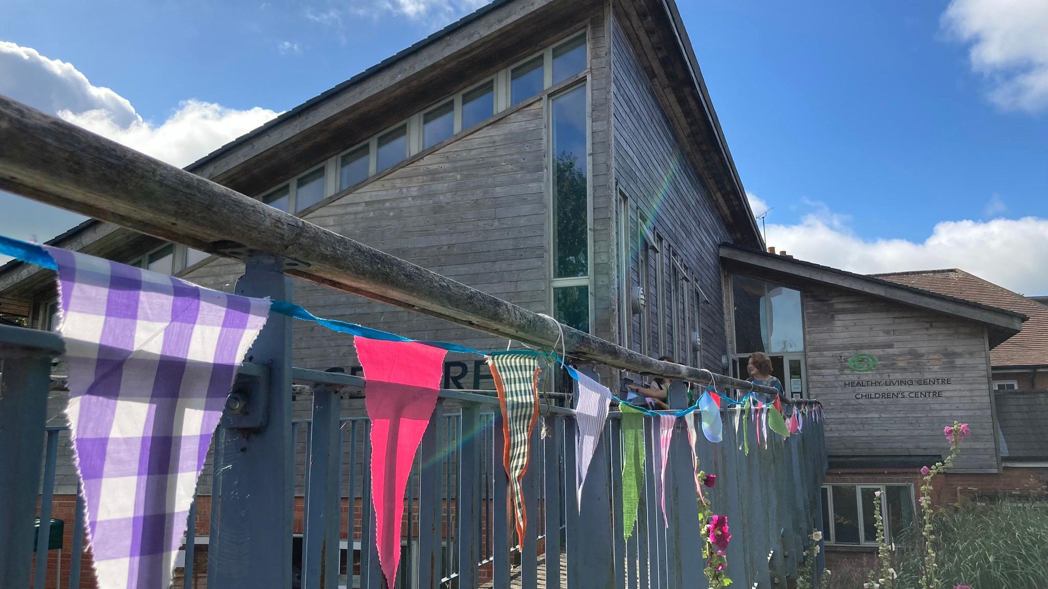 The Balsam Centre in Wincanton, Somerset. The buiding has a slanted roof with windows around the perimeter. A balcony can be seen, decorated with bunting.