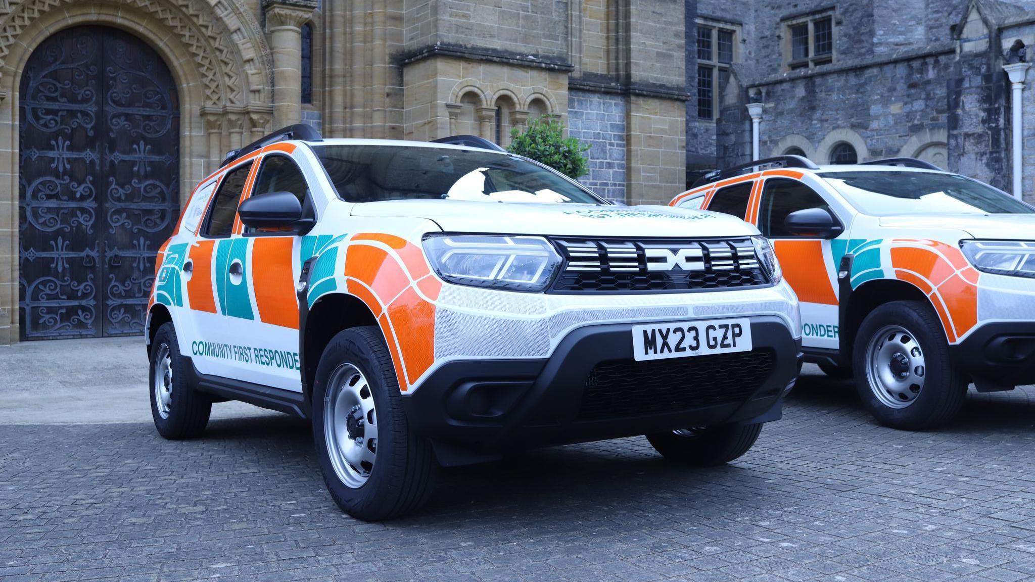 Two white Dacia cars with bright orange and turquoise Community First Responder livery