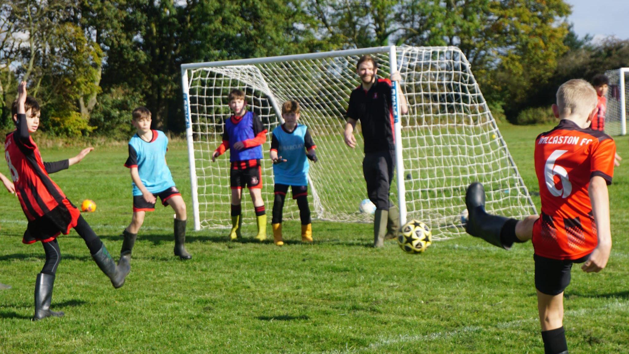 Children kicking a football at a goal in wellies