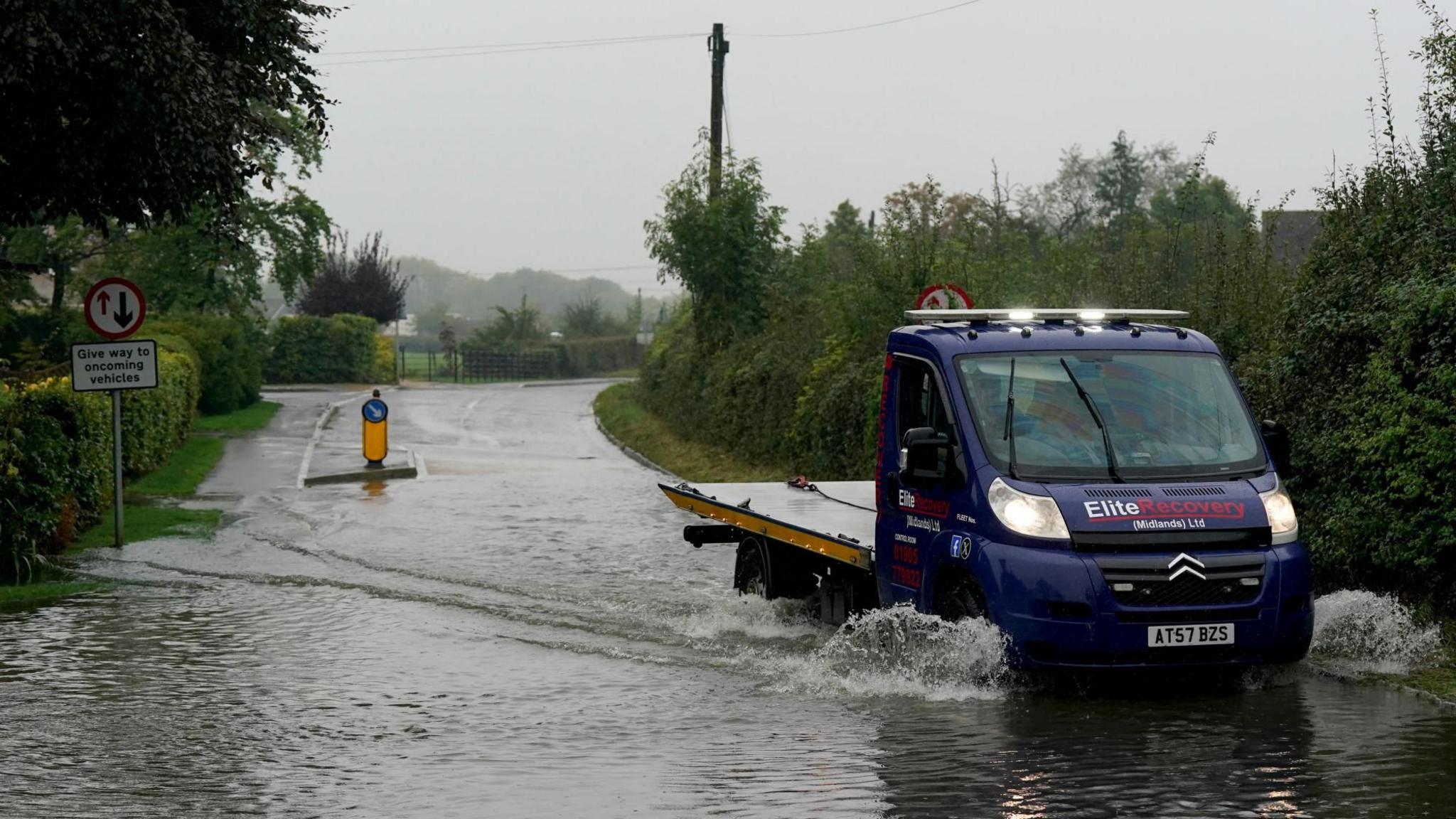 A vehicle drives through a flooded road in Willersey village, Gloucestershire.