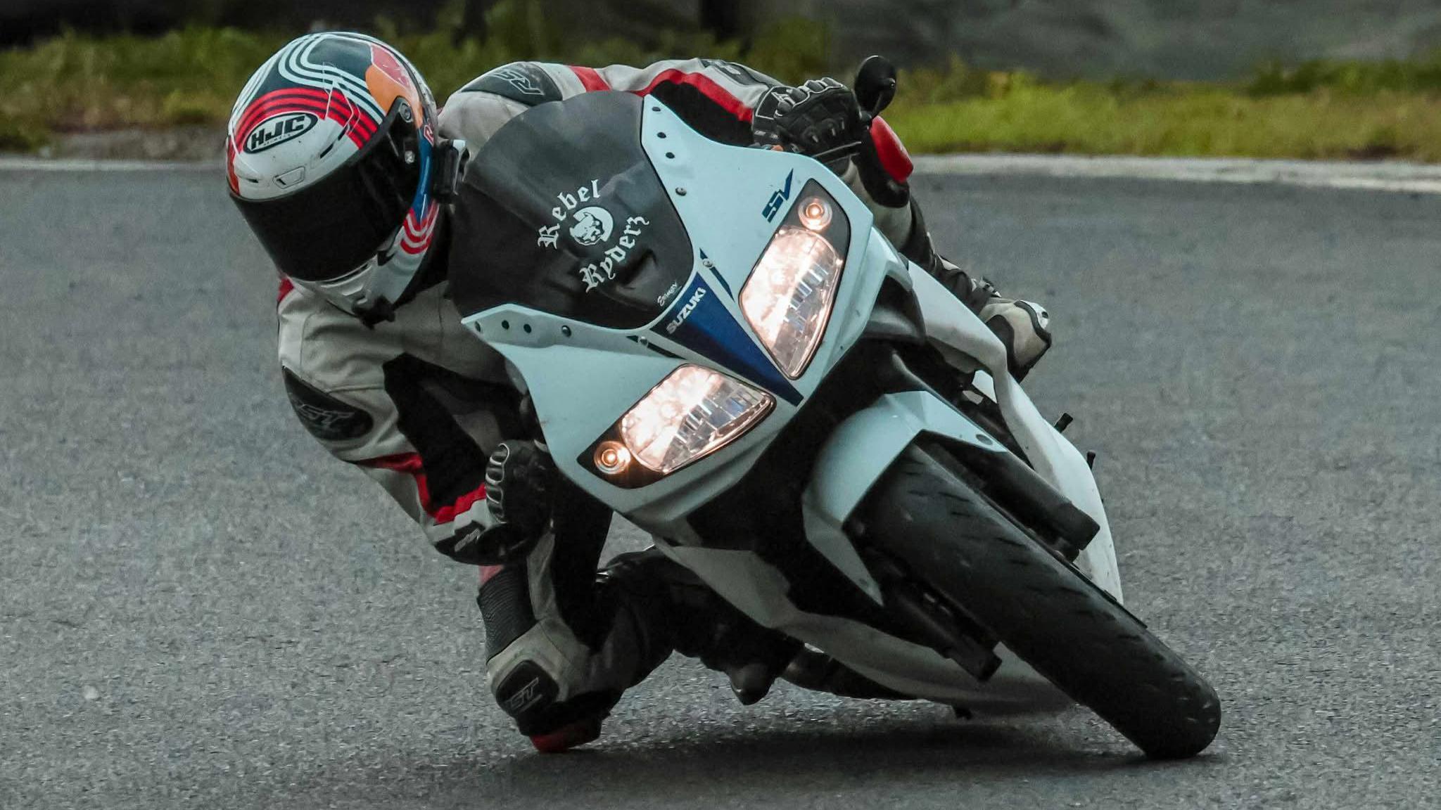 A motorcyclist is leaning into a corner. The motorbike is aqua and black. The motorcyclist is wearing a helmet and full leathers, all white, black and red.