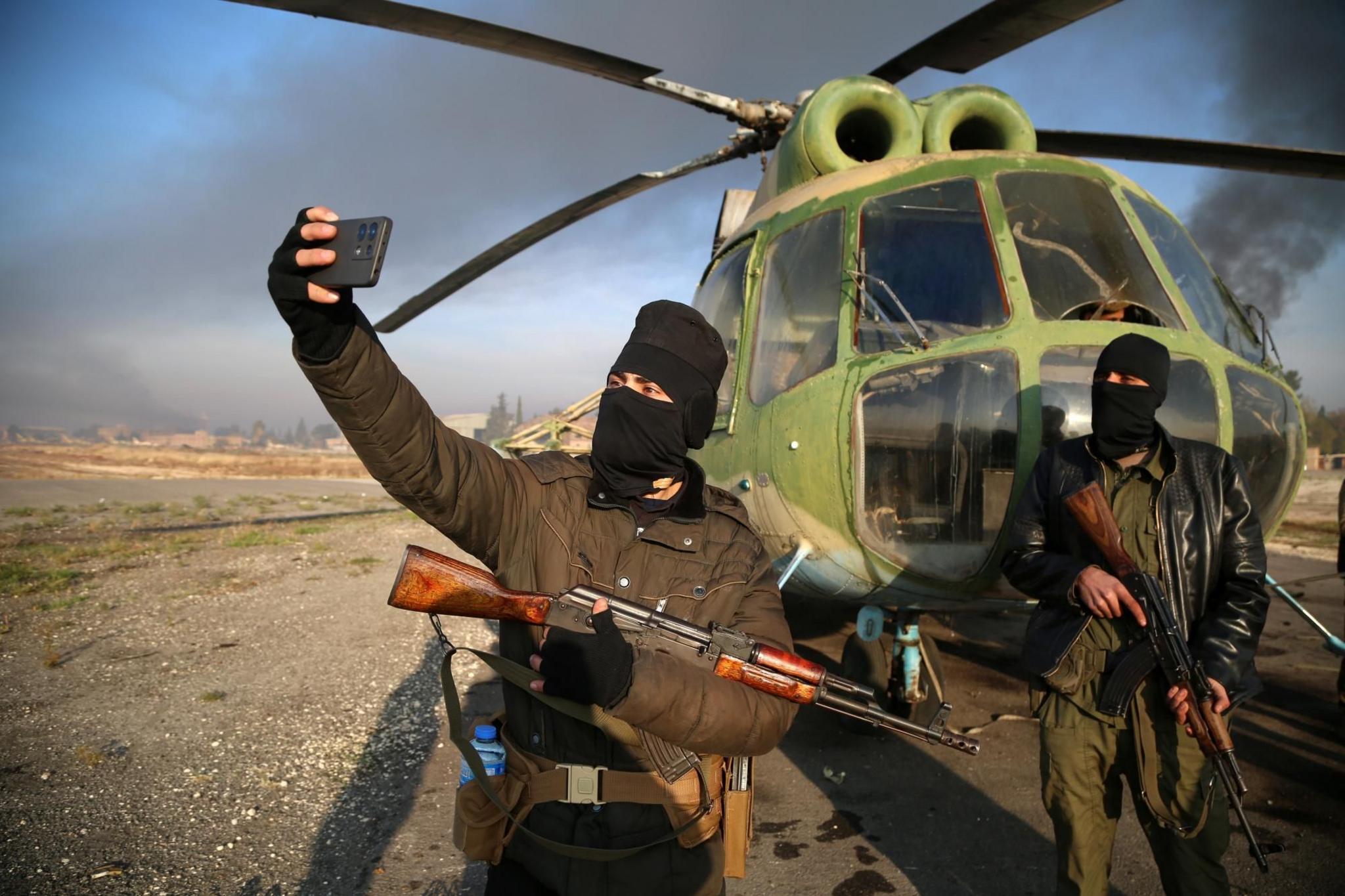 Armed men take selfies at the Nayrab military airport, in Aleppo, Syria
