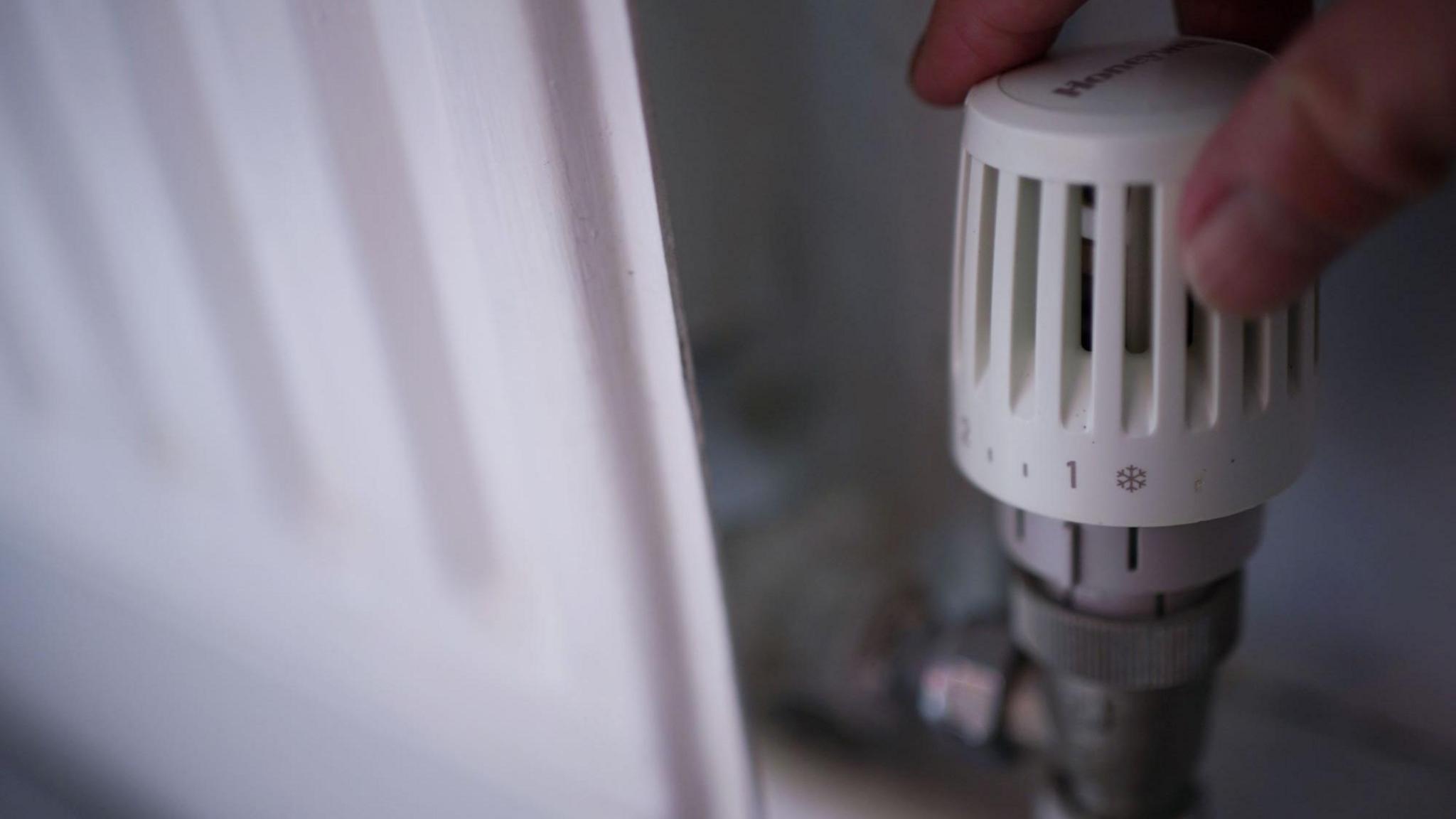 Hand on a thermostat on a white radiator 