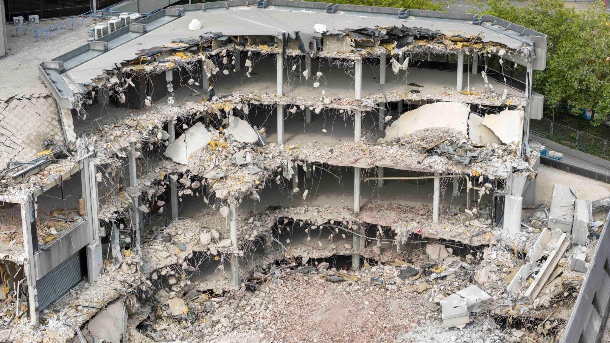 An aerial image of the demolition site, showing three buildings remaining standing and an area of land that is destroyed where the former buildings stood.