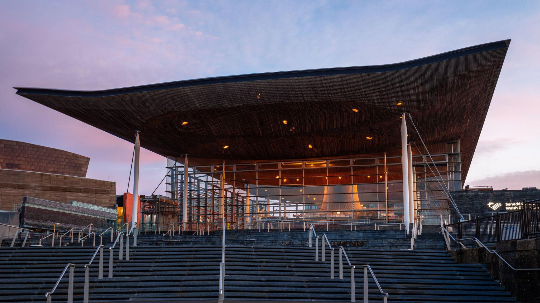 The Senedd building - a glass front with a large roof canopy over steps to the entrance.