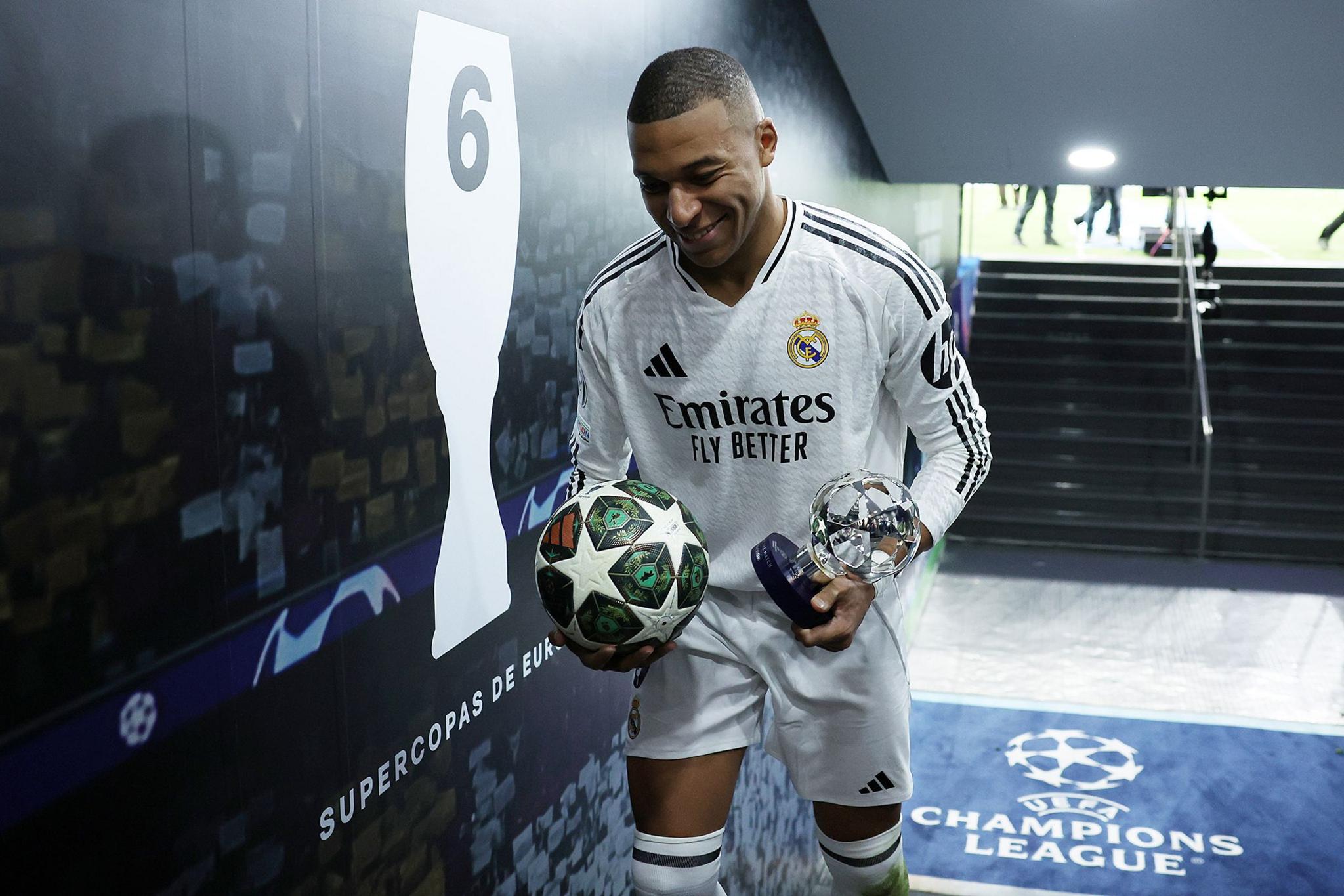 Real Madrid forward Kylian Mbappe smiles while carrying the Player of the Match trophy and match ball after scoring a hat-trick during the Champions League  match against Manchester City at the Bernabeu