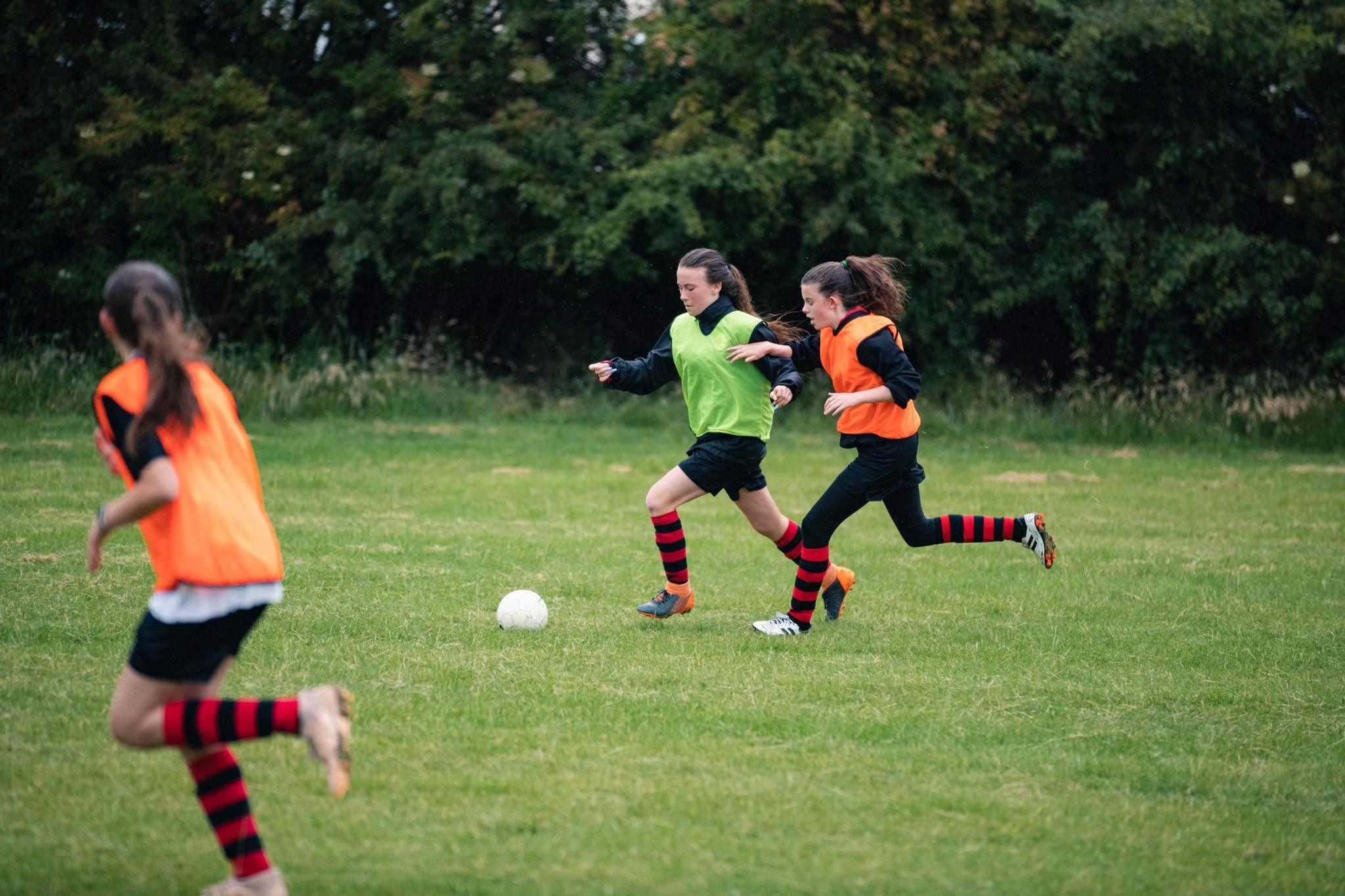 Two girls from opposing teams chase the ball during football training. 