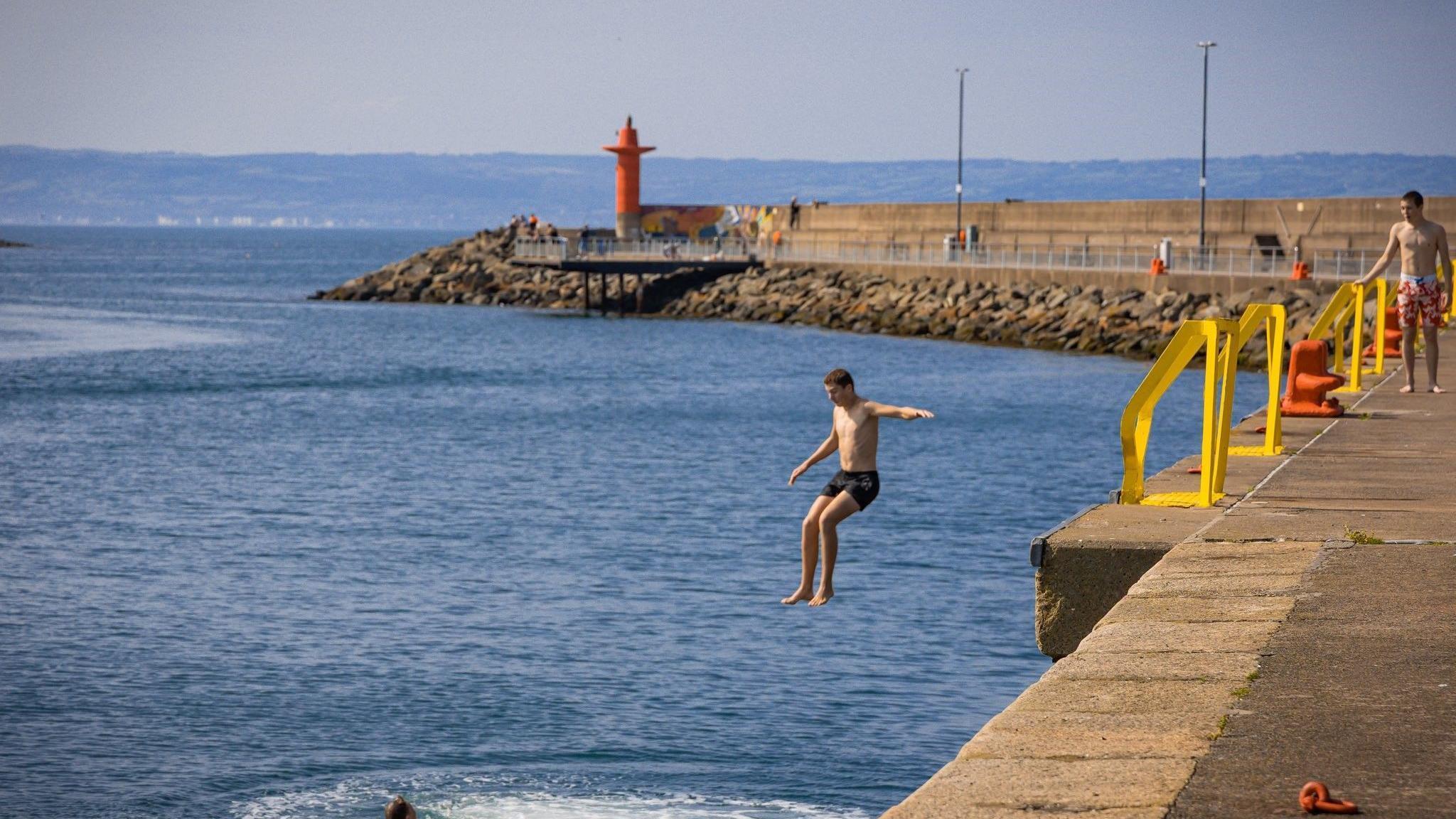 A man jumps into the water on a sunny day at a pier. 