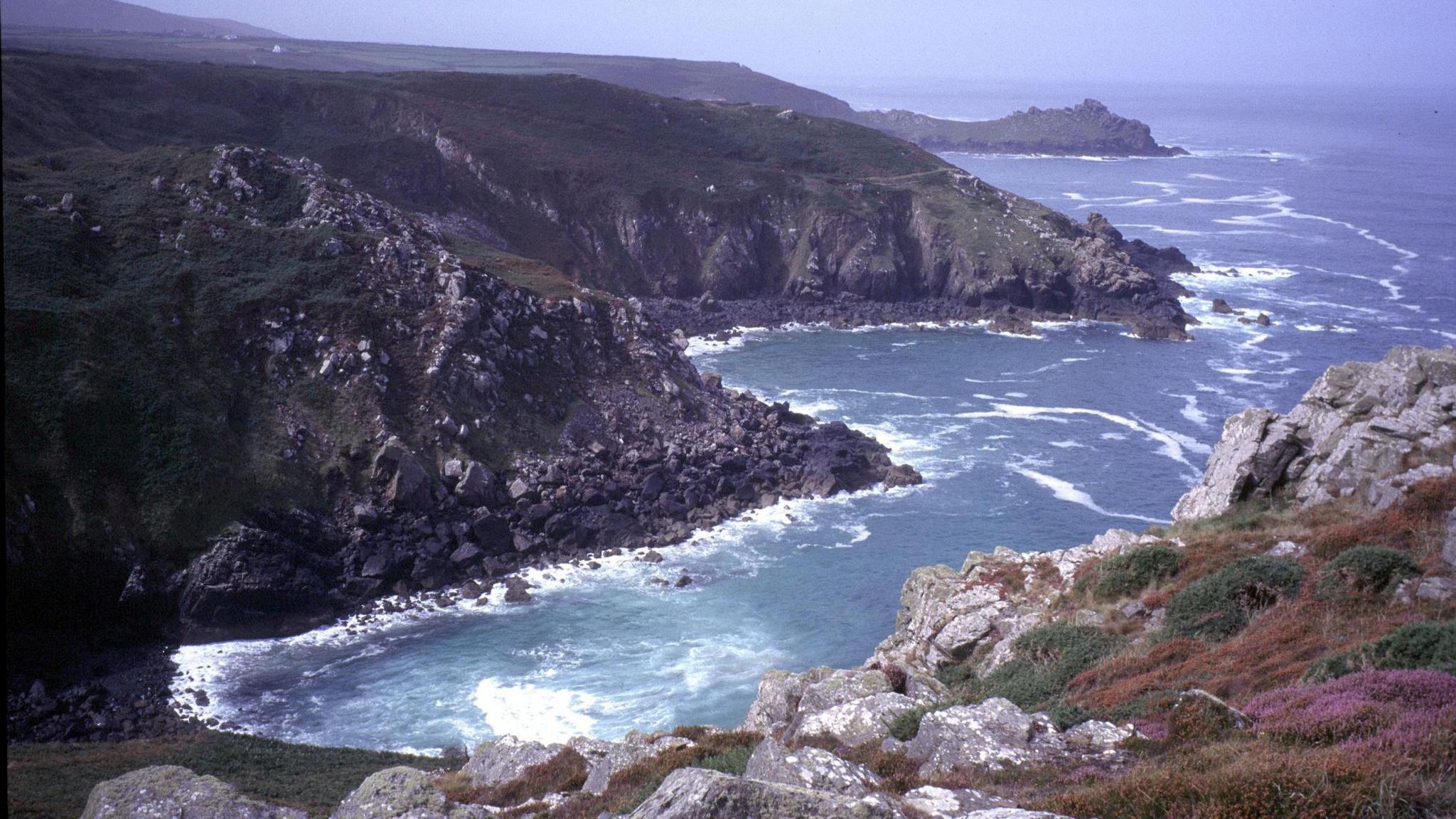 The photograph shows a stormy coastline in Cornwall. There are waves crashing into the rocks below while the photographer is positioned at the top of the cliff looking down. 