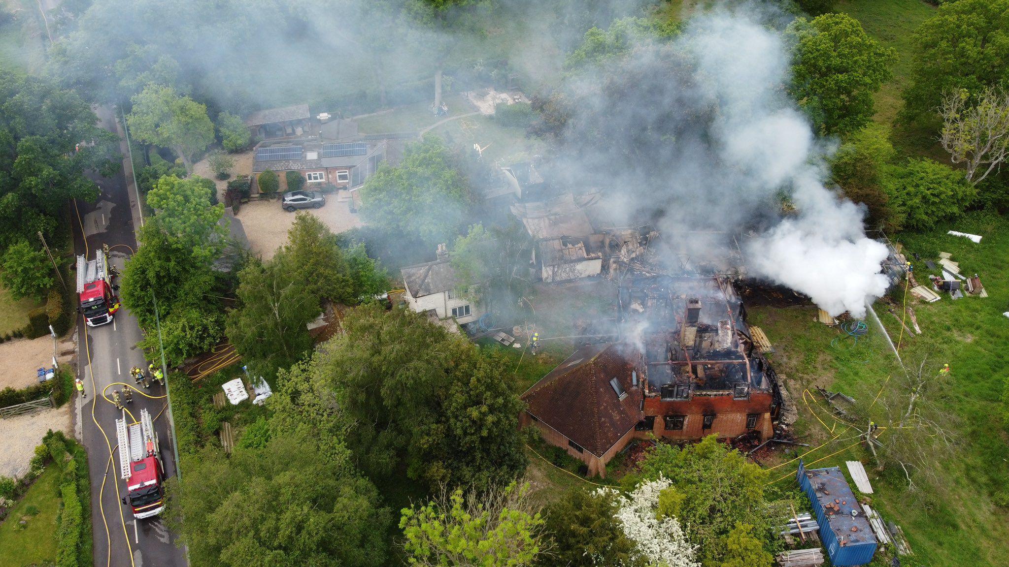 A house surrounded by trees is charred and burnt as smoke billows into the sky.