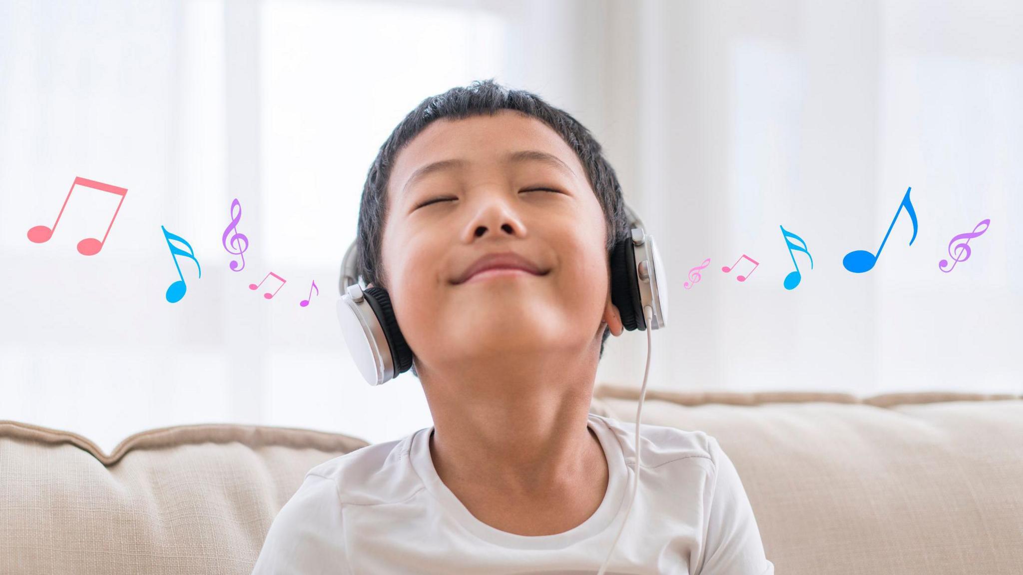 A boy with headphones on smiling with his head up in the air. There are colourful music notes coming out of either ear