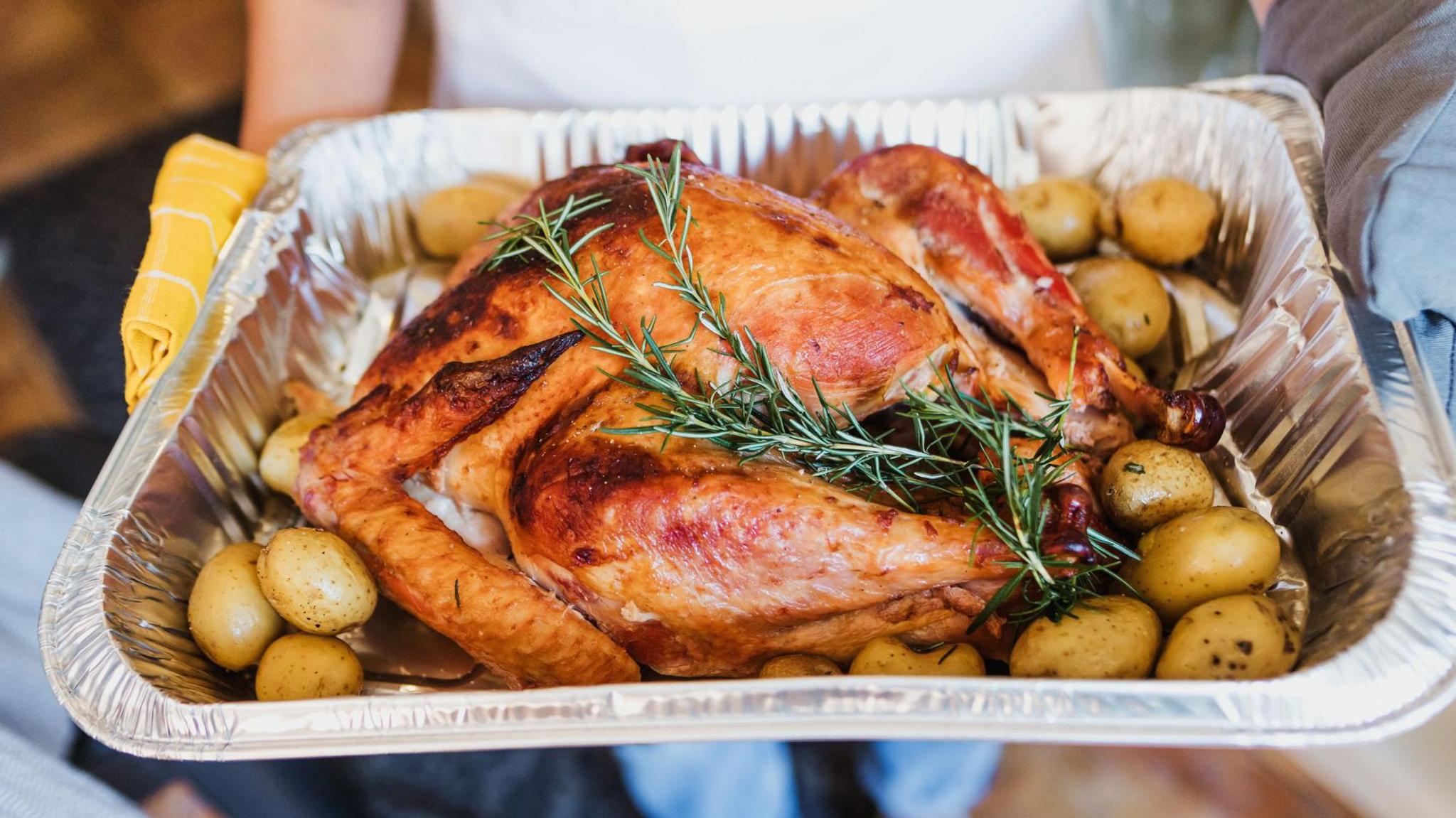 A cooked turkey in a silver tray with potatoes and herbs around the side.