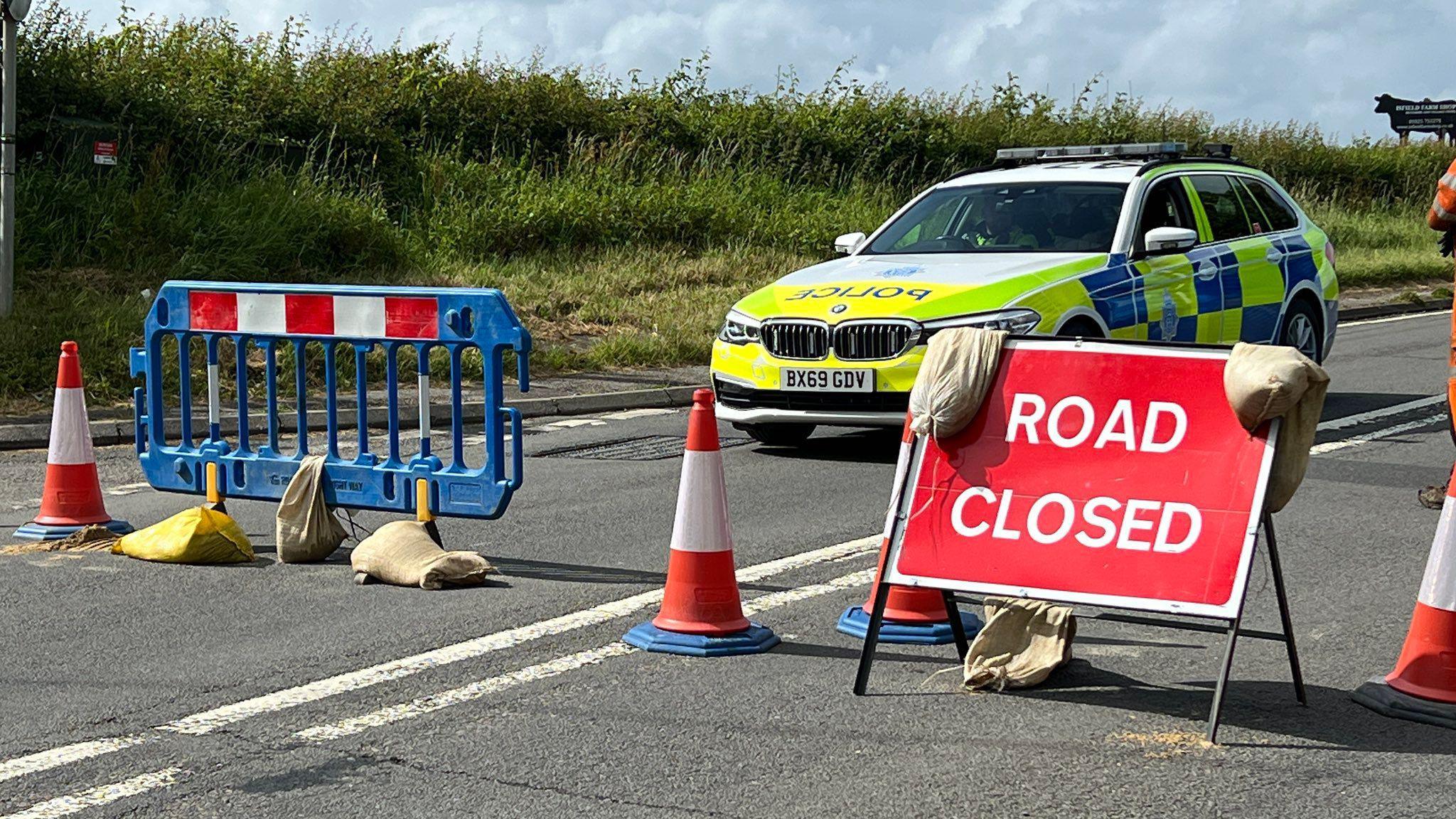 A police car next to a red sign reading Road Closed