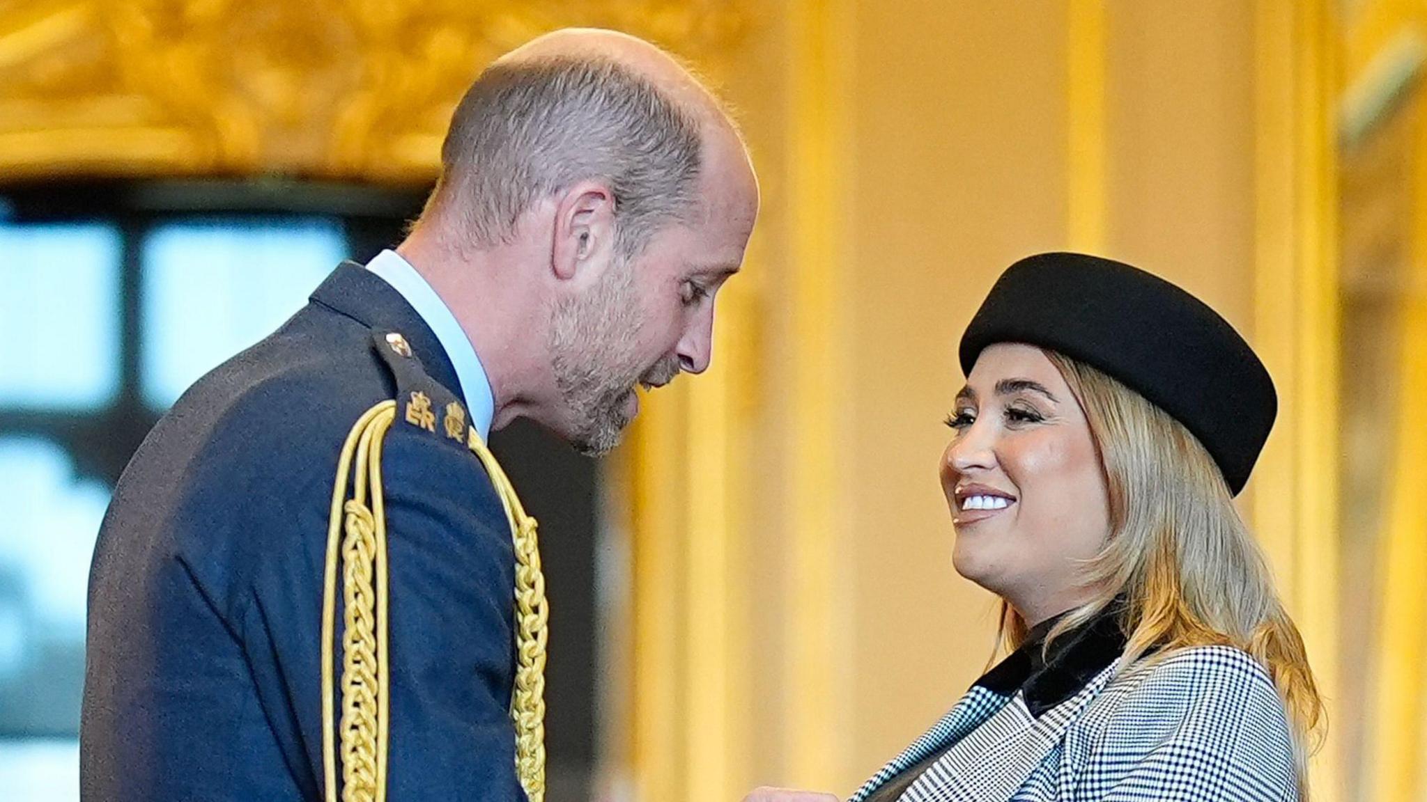 Prince William honouring Georgia Harrison with a MBE. They are both smiling.