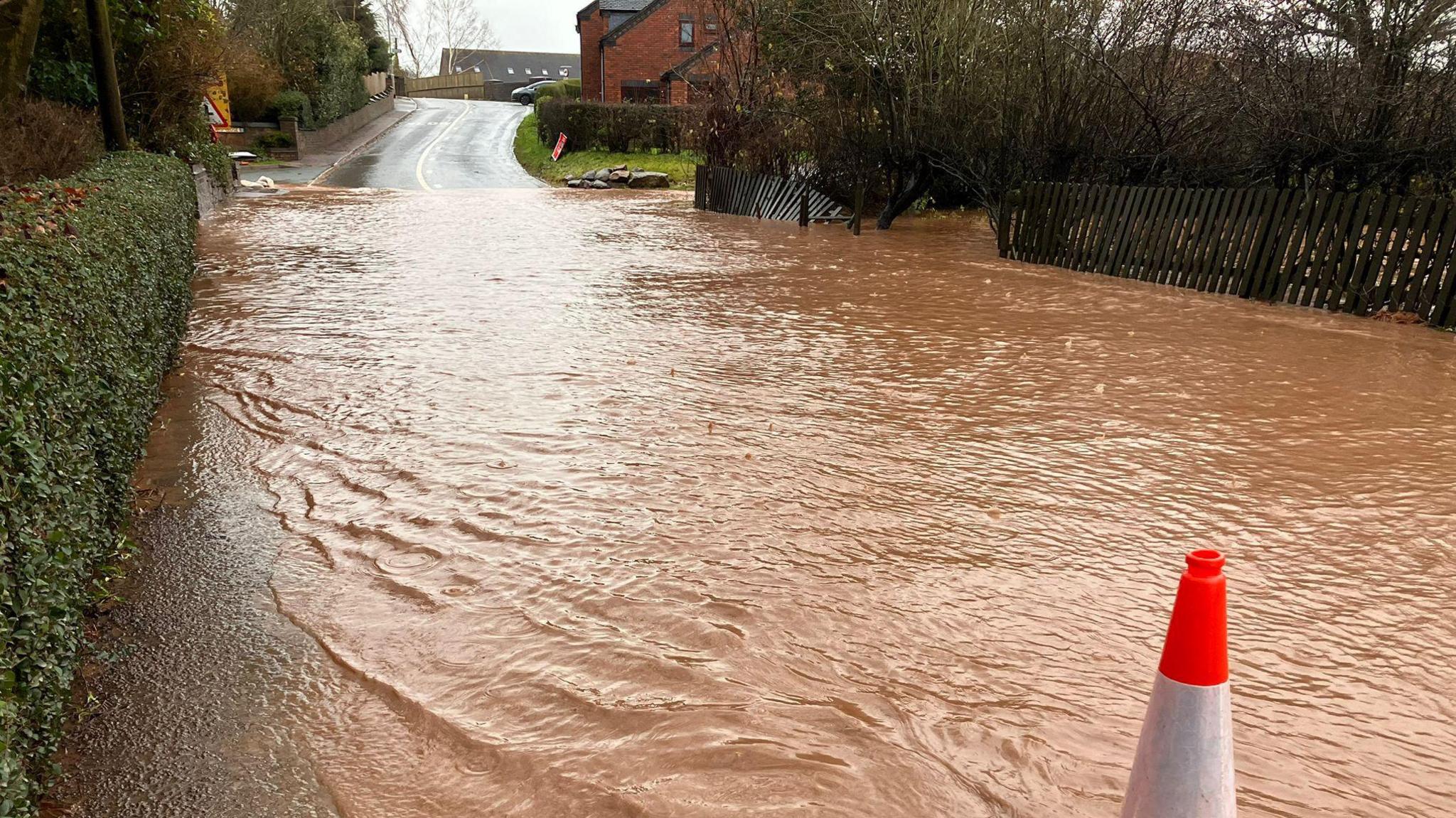 Brown water covering a road with a fence knocked down on the right hand side