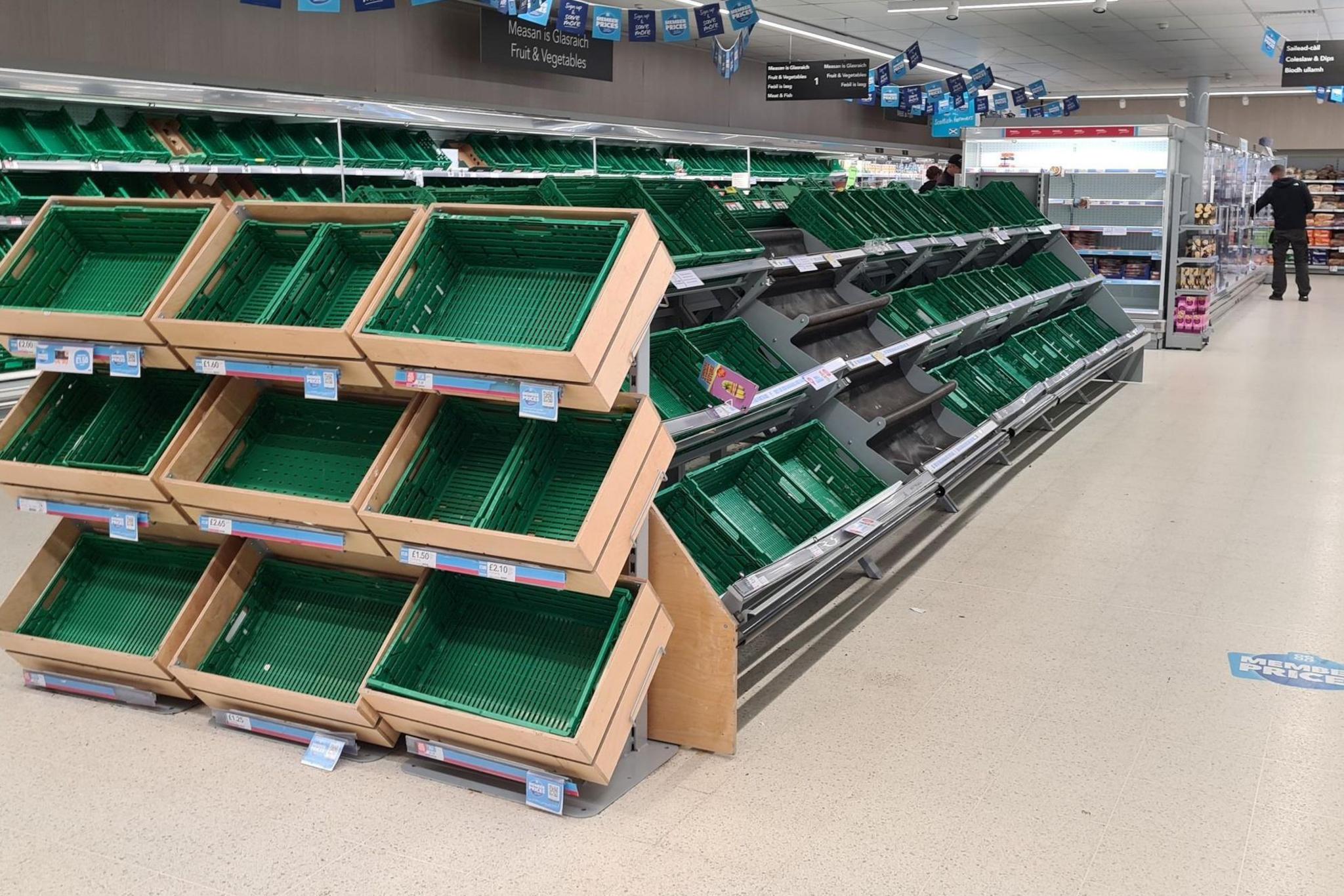 Empty green plastic boxes for fresh produce. There is a shopper browsing products in the background.
