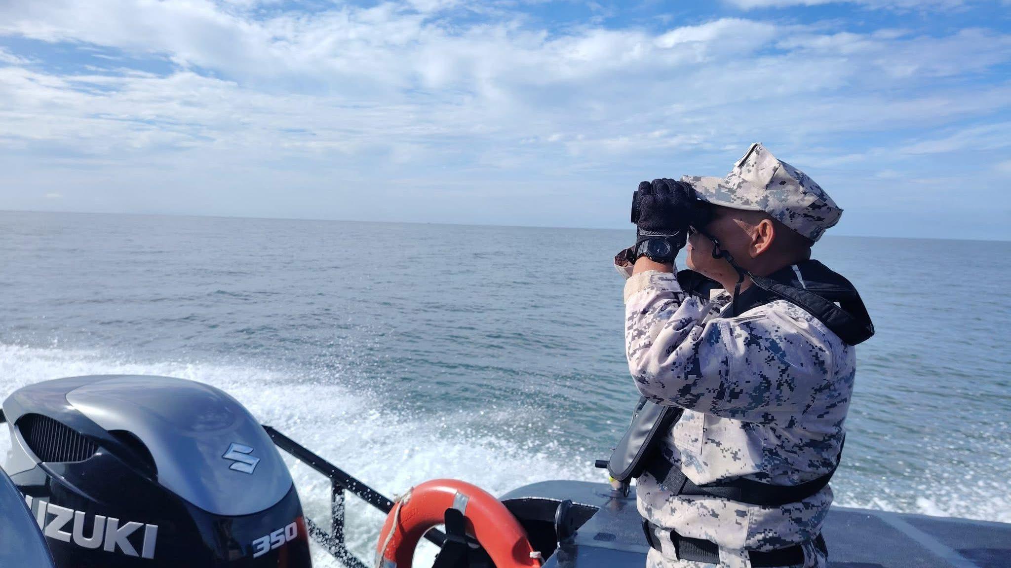 A Malaysian Coast Guard official on a boat uses binoculars to search the water