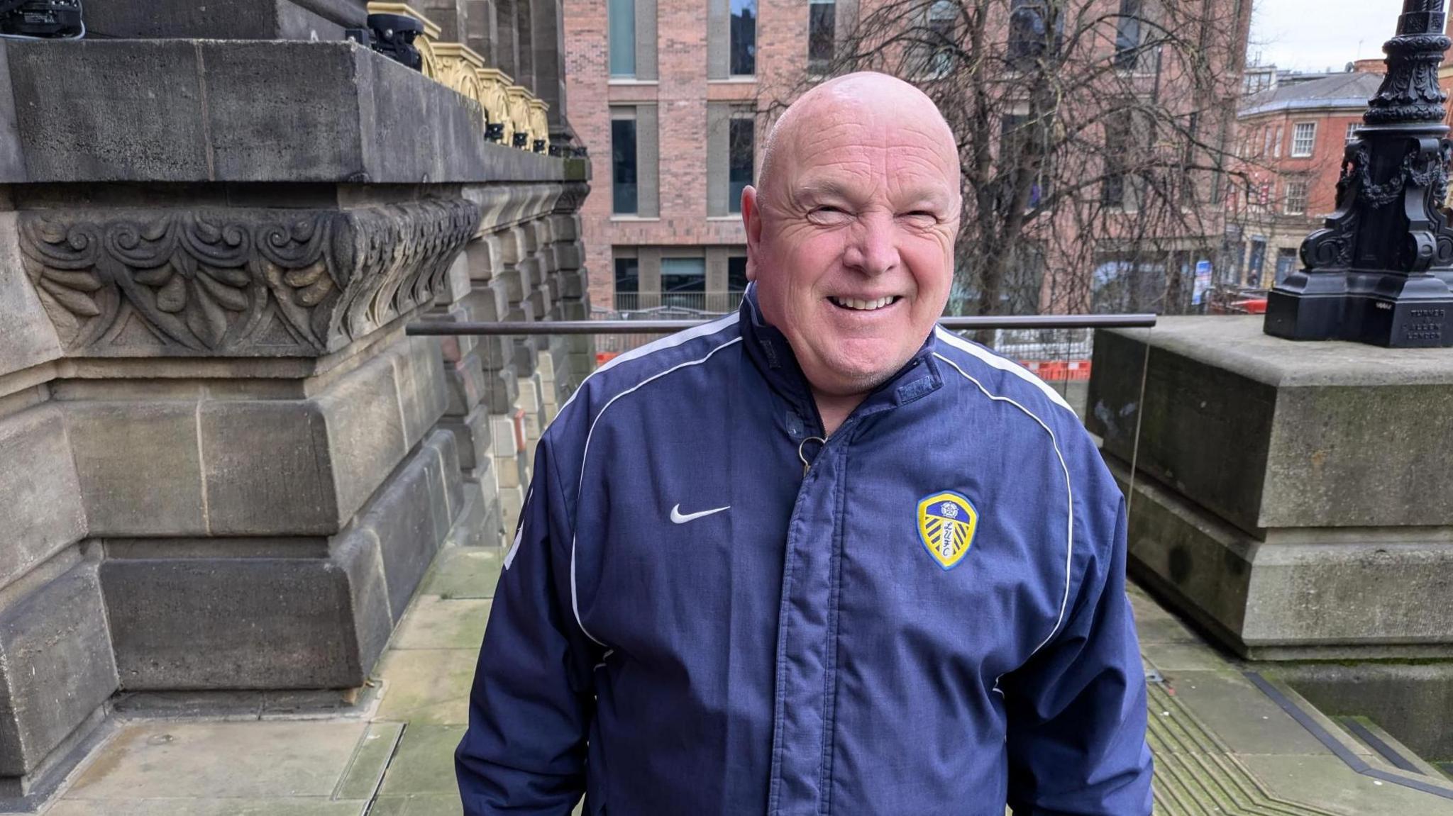 A middle-aged man smiling into the camera. He is wearing a Leeds United tracksuit 