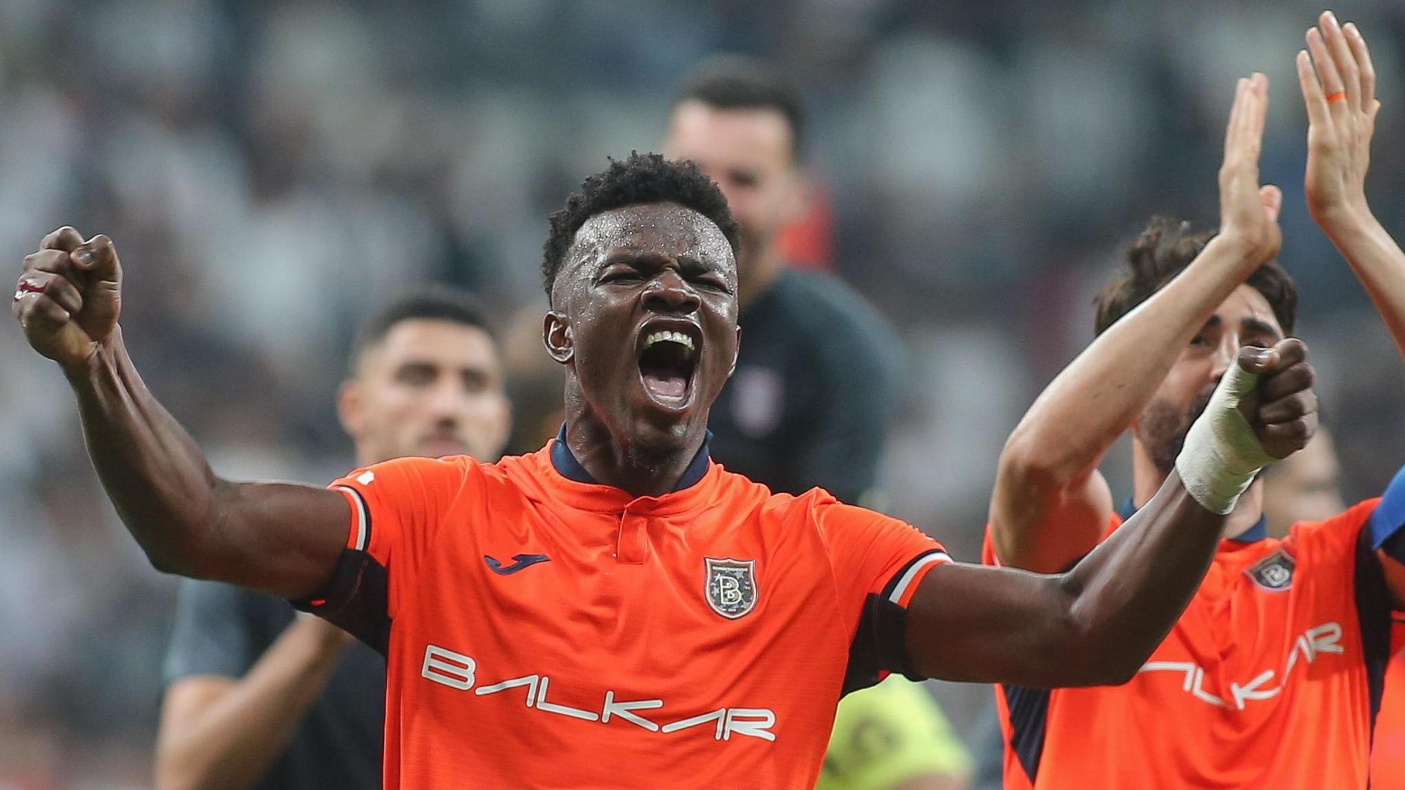 Youssouf Ndayishimiye in an orange kit spreads his arm wides and screams in celebration after a game with Istanbul Basaksehir