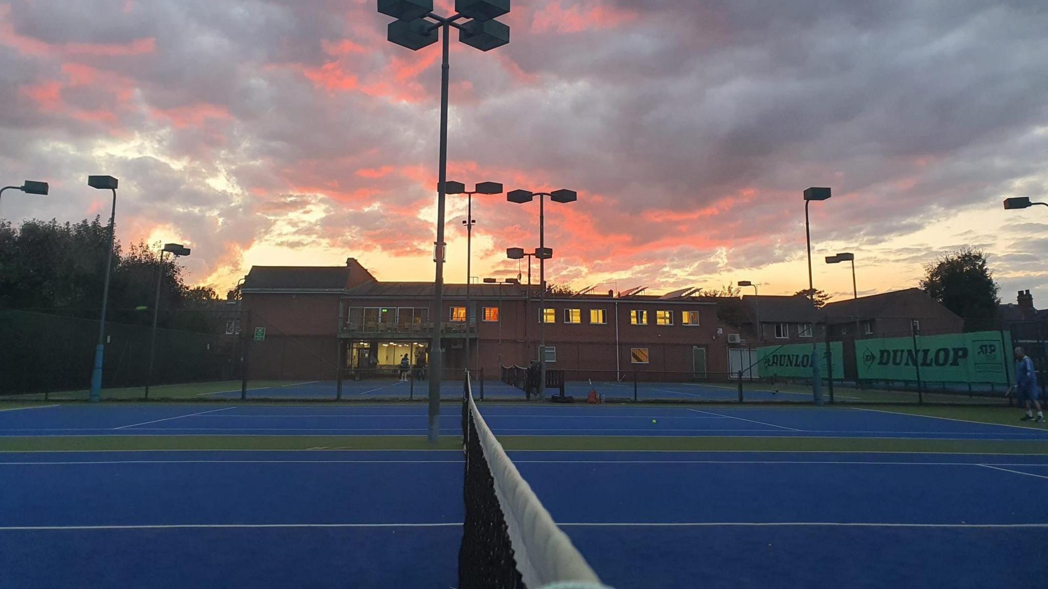 Tennis courts at dusk with a building in the background 