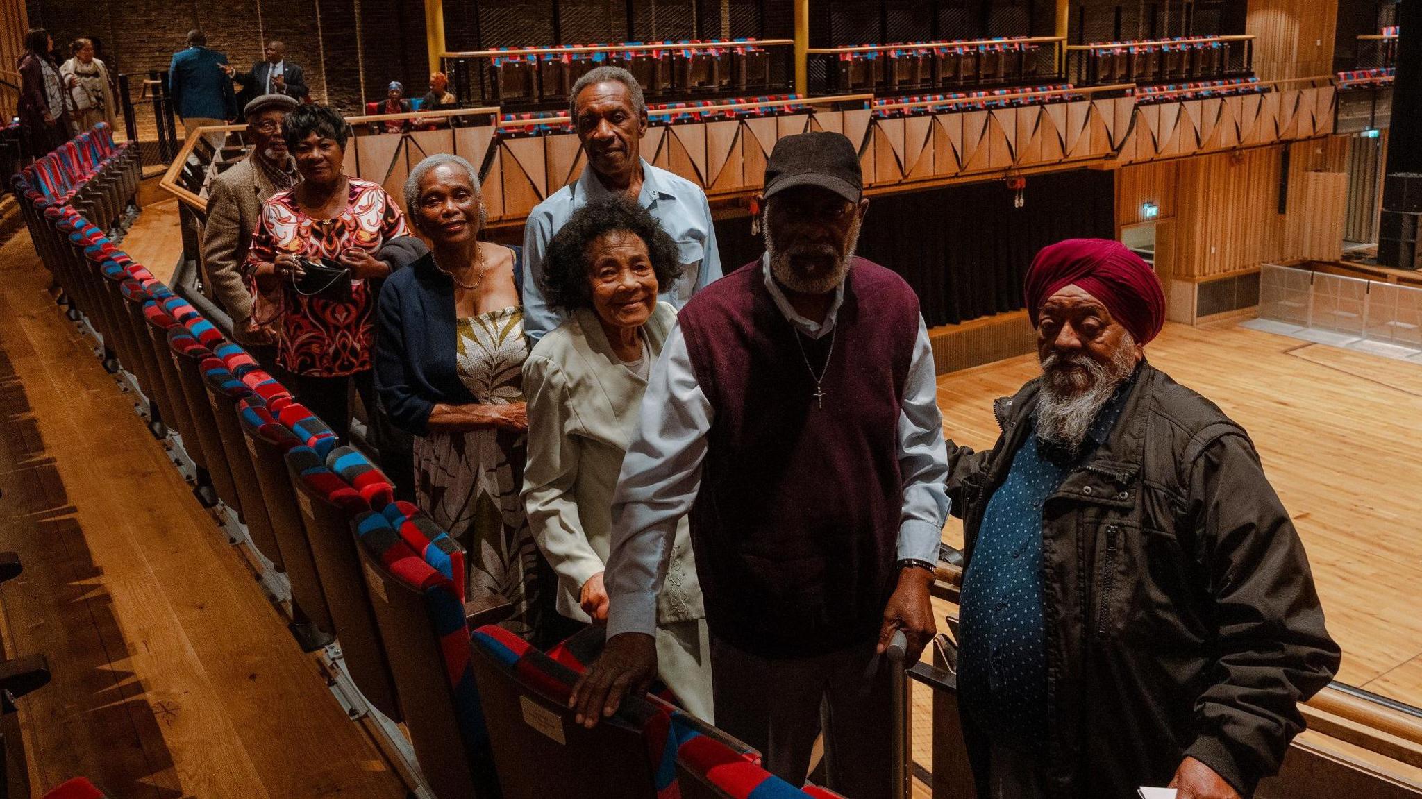 A group of civil rights activists face the camera during a ceremony to honour people who took part in the Bristol Bus Boycott. In the background the main Bristol Beacon auditorium is visible