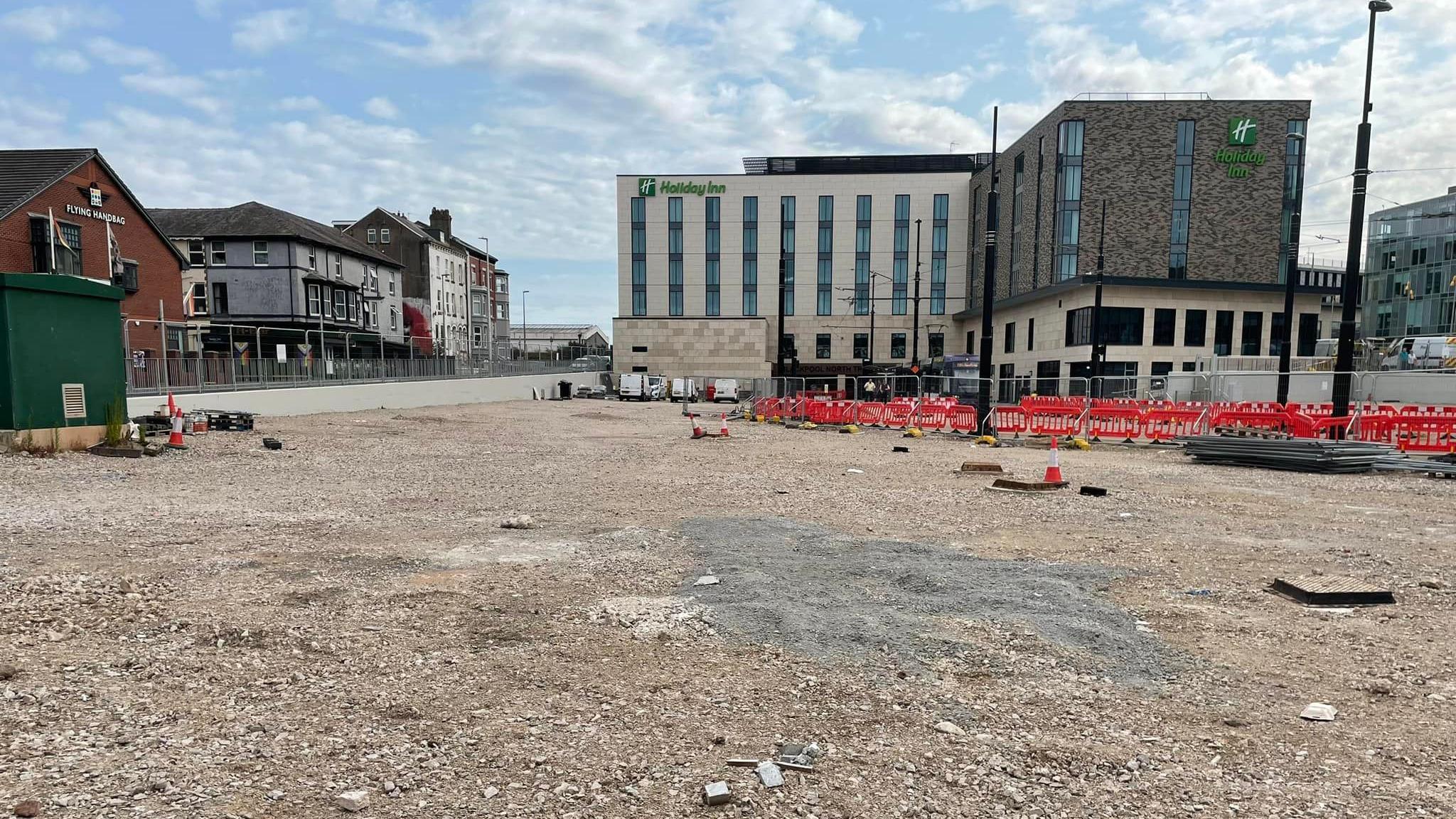 An empty piece of land with traffic cones on and The Holiday Inn hotel in the background