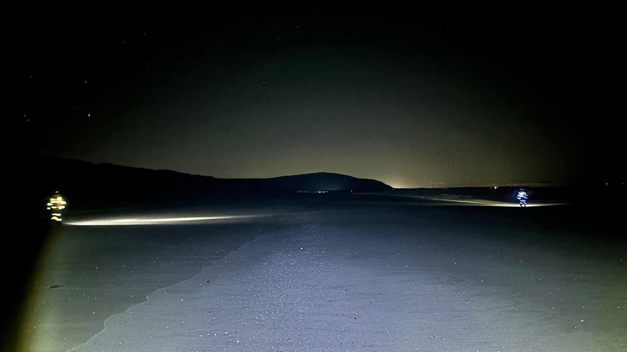 Search lights on the beach at night with two of the rescue team scouring the area