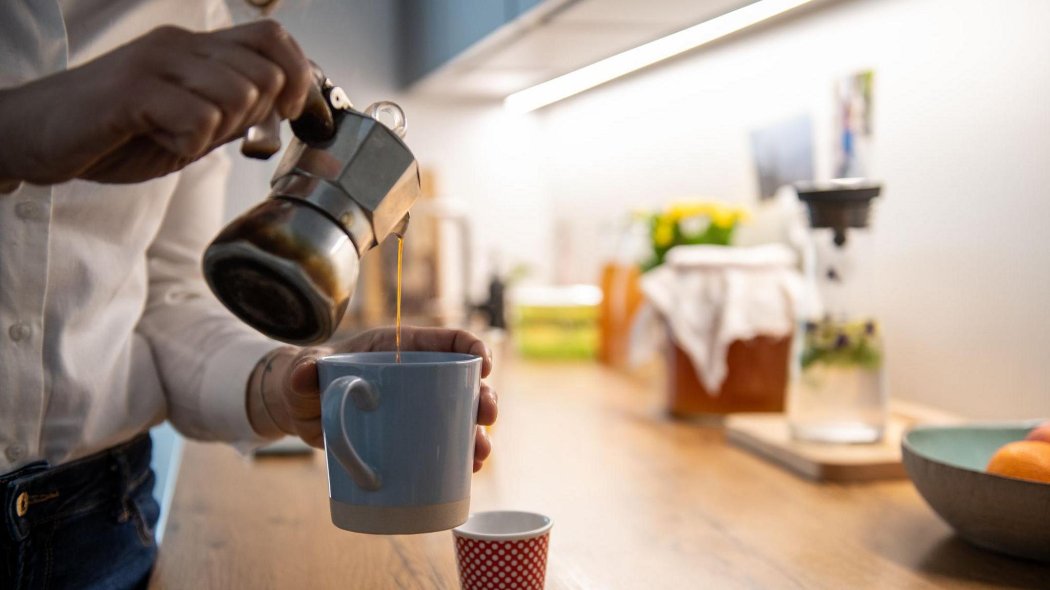 Male hands pouring coffee in a white mug at night time