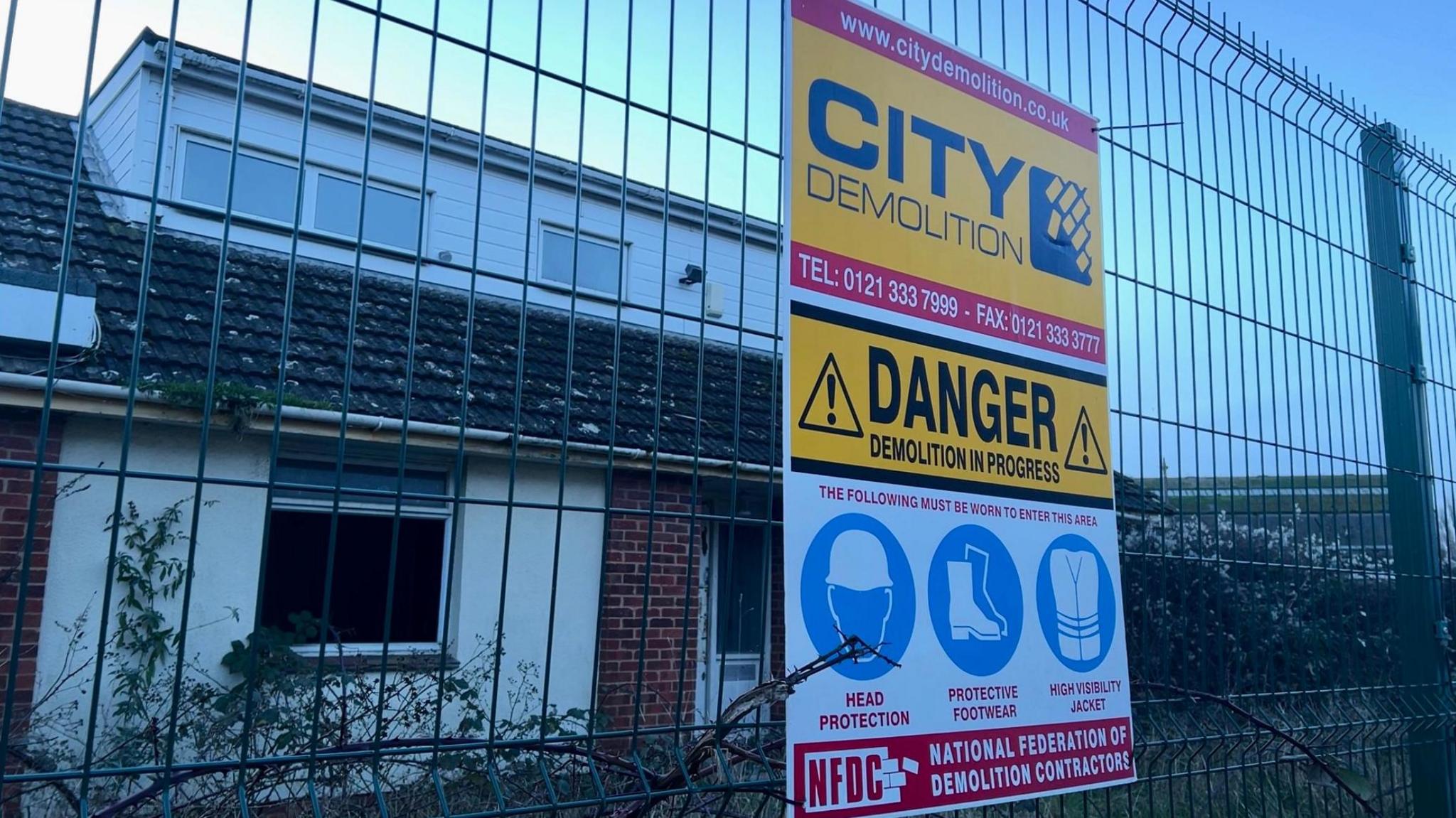 A demolition sign on a fence at the front of a derelict house on the Water Lane site in Exeter