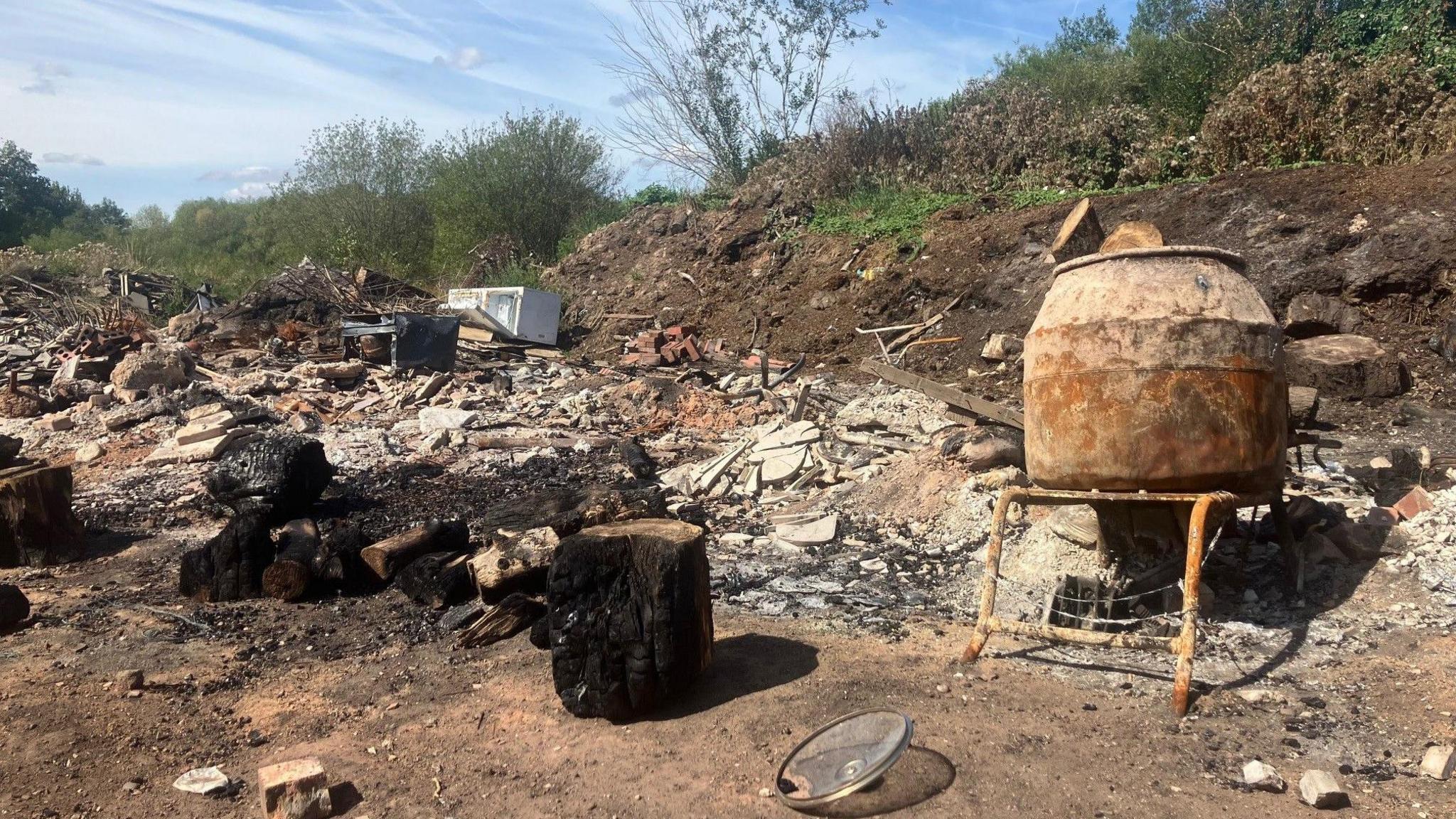 Photograph of charred waste - after a fire at a suspected illegal waste dump near the River Mersey in Greater Manchester. The image shows the charred remains of waste.