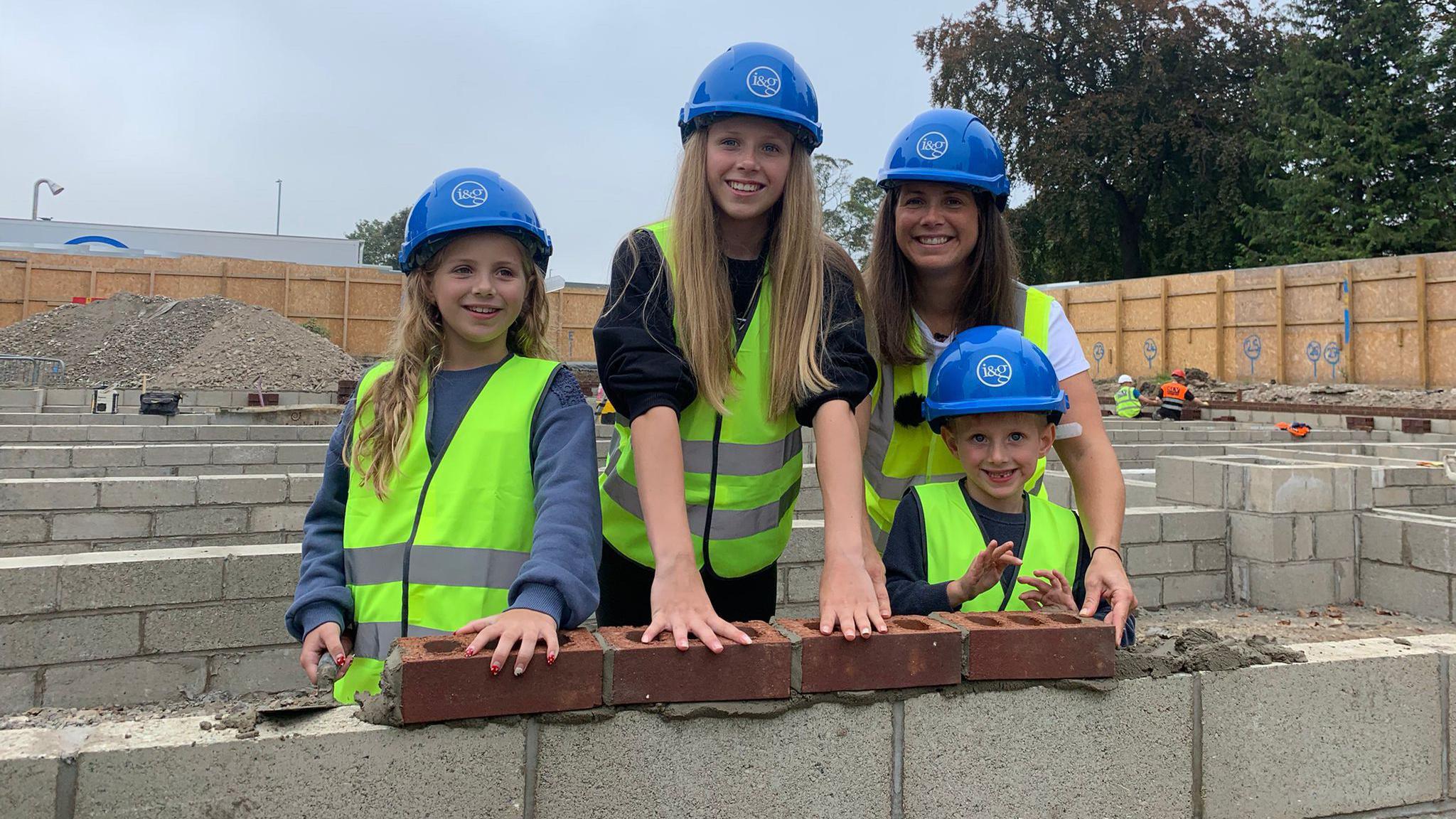 Rob Burrow's wife and three children wear high vis jackets and hard helmets as they lay bricks on the Motor Neurone Disease Centre in Leeds.