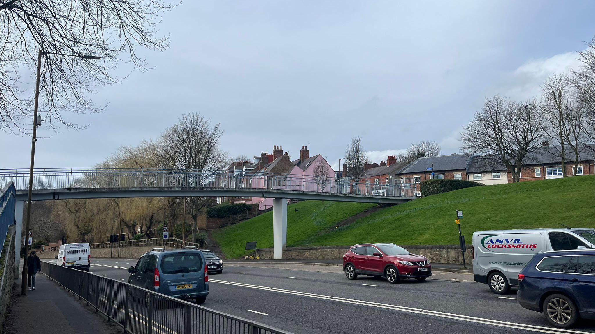 Vehicles travel in both directions on the A690. The pedestrian footbridge straddles four lanes.