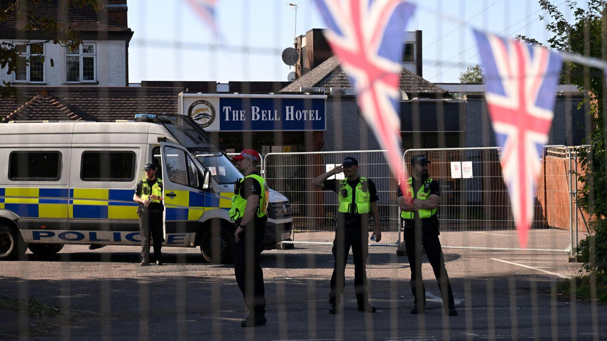 Police officers guarding The Bell Hotel in Epping. They have been pictured behind a fence with Union Jack flags in the foreground.